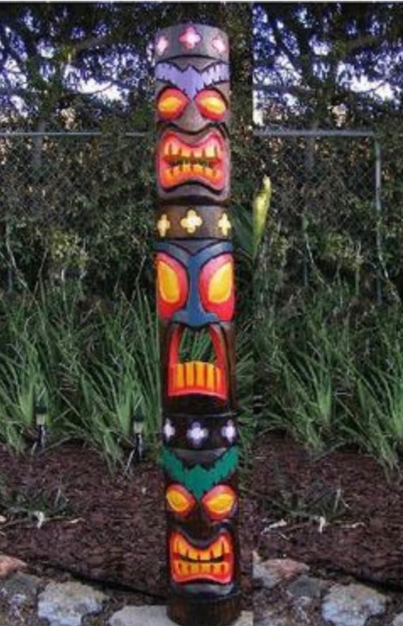 Tall colorful tiki totem pole with multiple faces in a garden setting