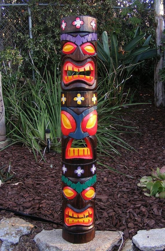Colorful carved tiki totem pole with floral designs in a garden