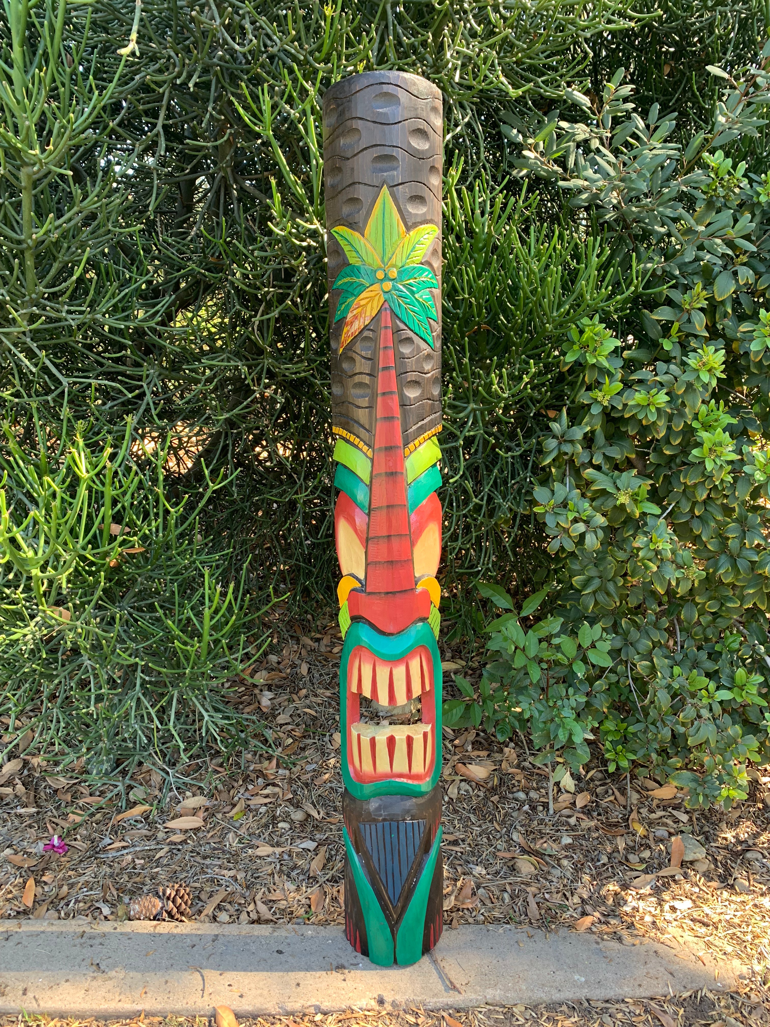 Colorful tiki totem pole painted with a palm tree design in a garden