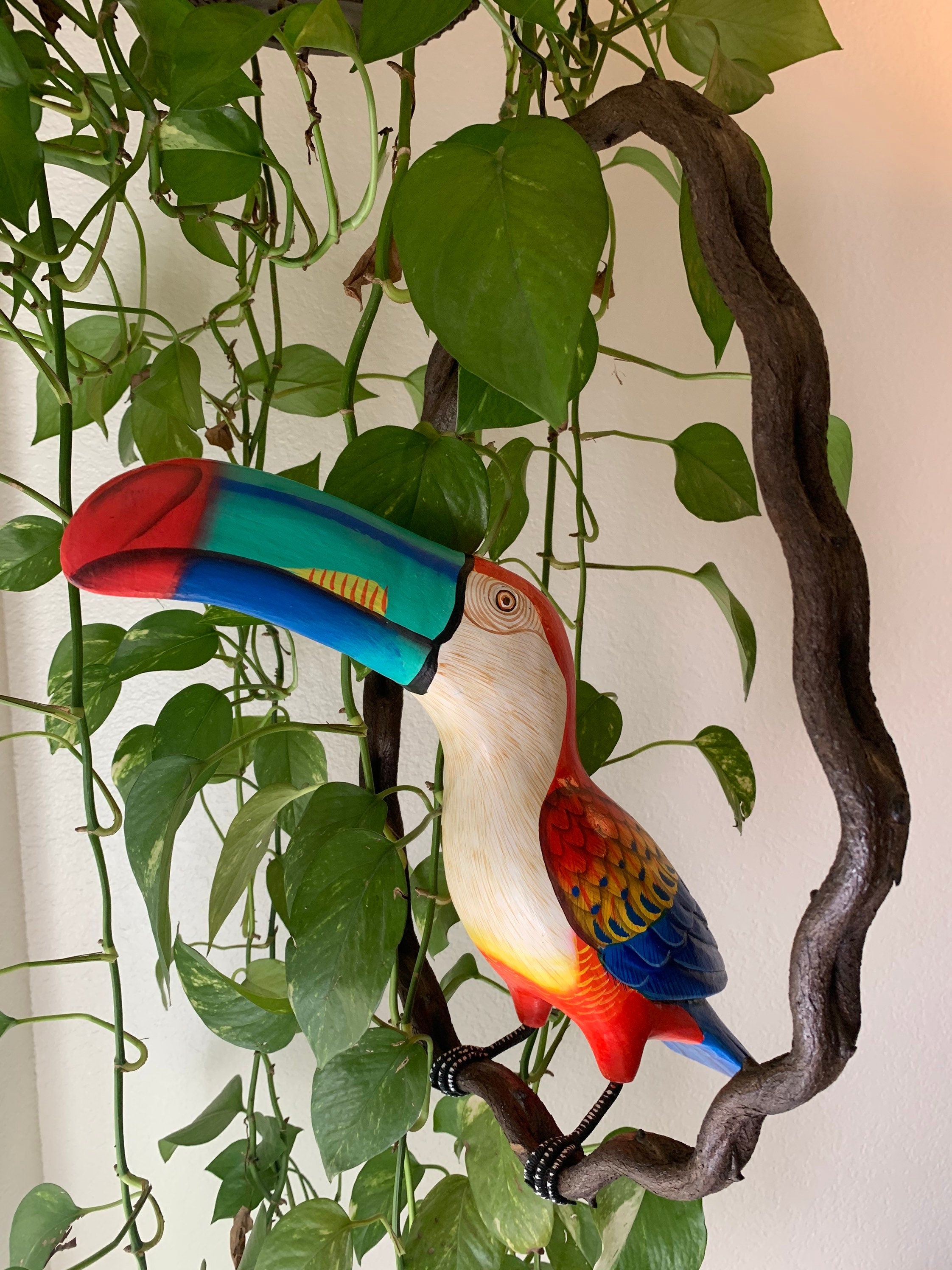 Colorful toucan sculpture perched on a twisted branch among green pothos vines
