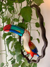 Colorful toucan sculpture perched on a twisted branch among green pothos vines