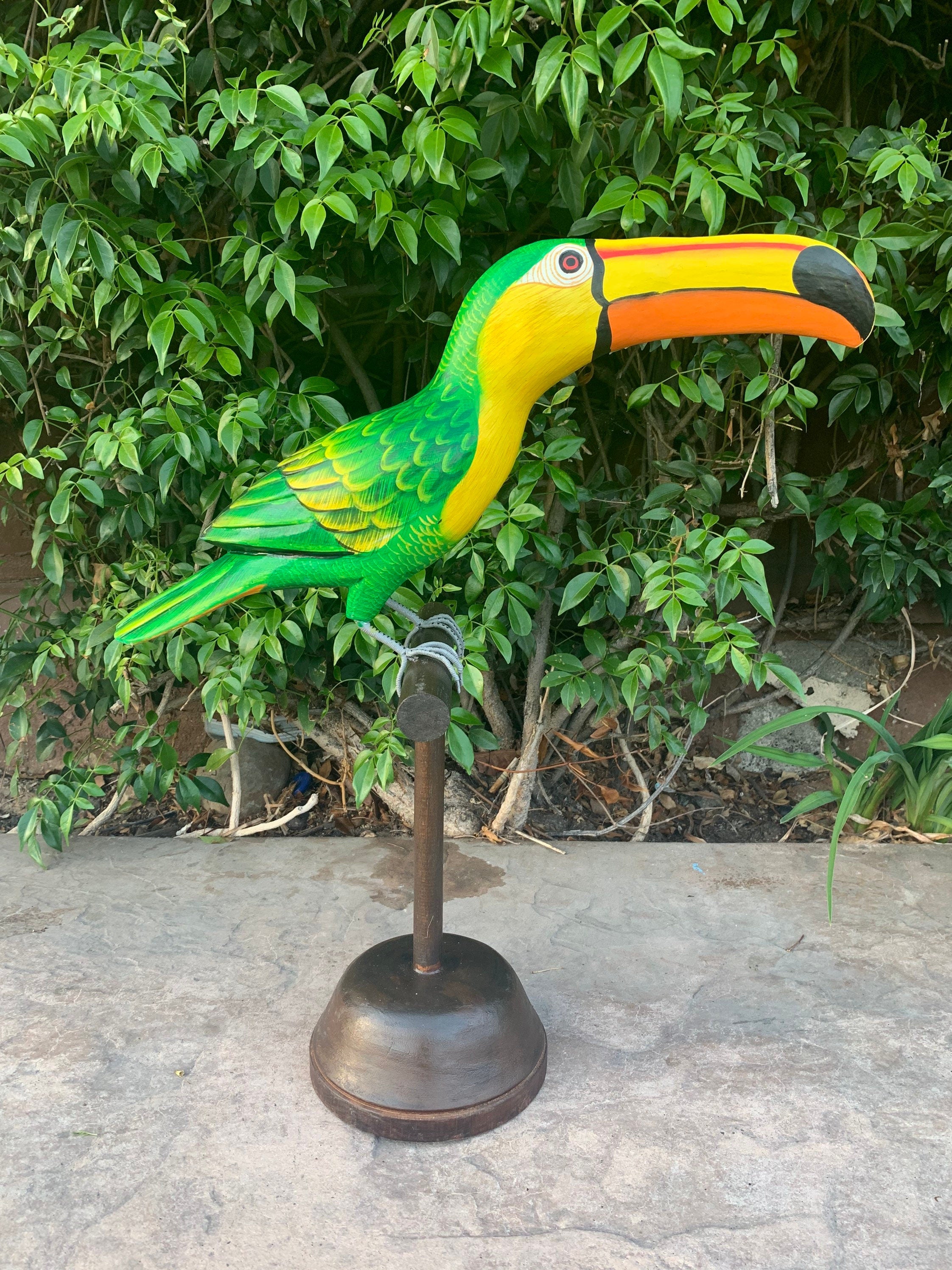 Colorful toucan statue perched on a metal stand in a garden