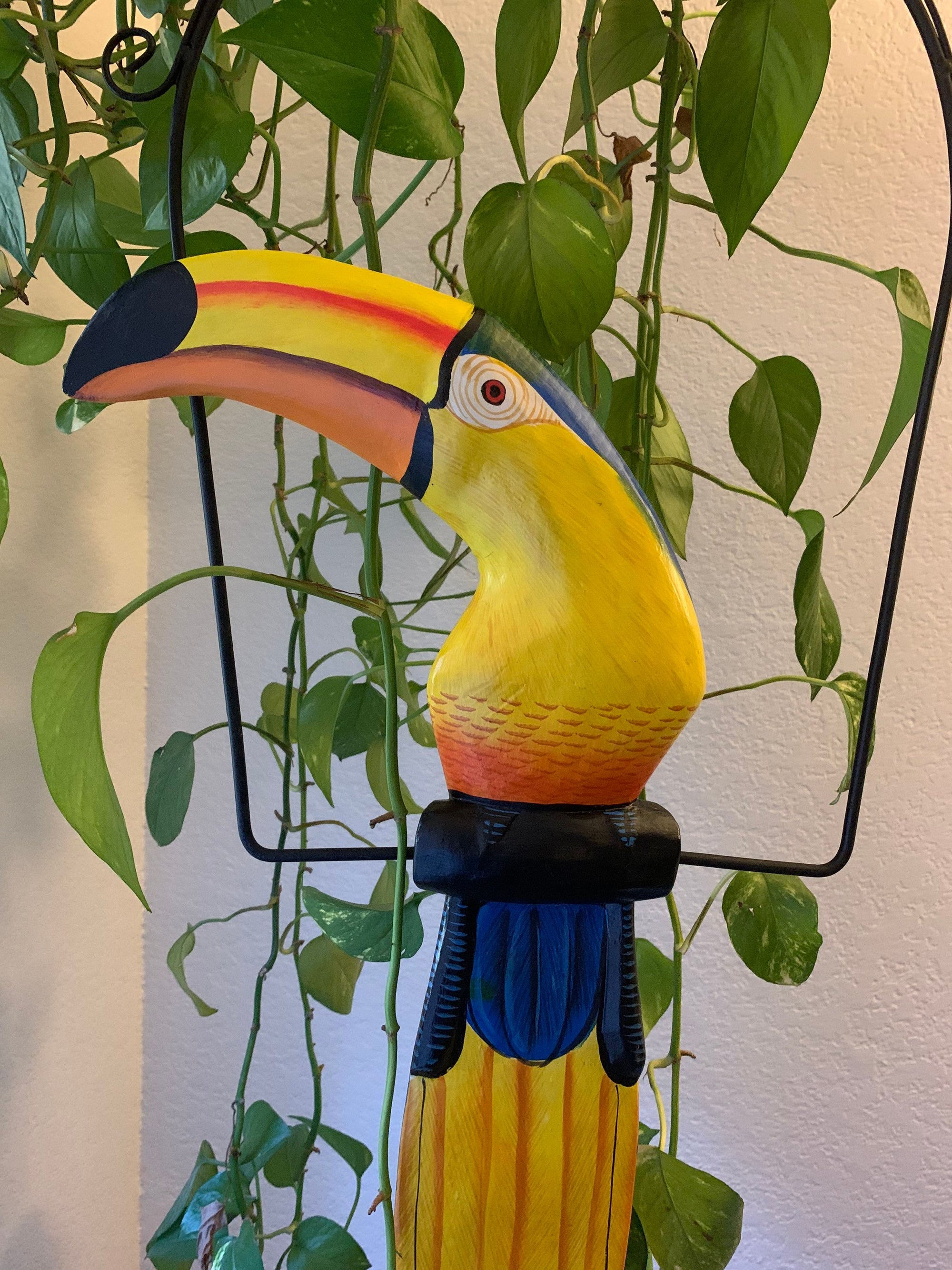 colorful toucan sculpture with yellow beak among green houseplants