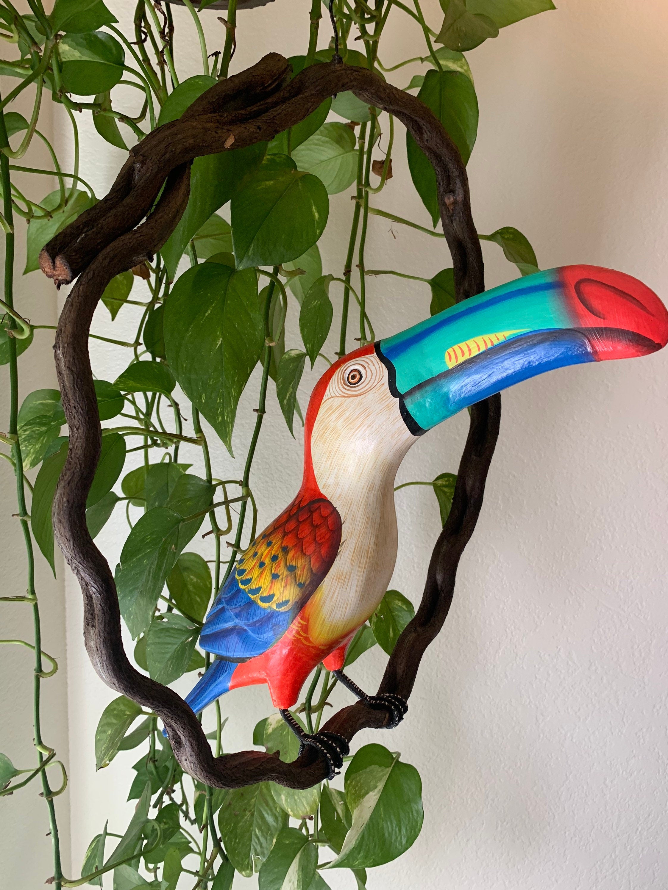 Colorful toucan sculpture framed by a dark wooden loop with green leafy vines