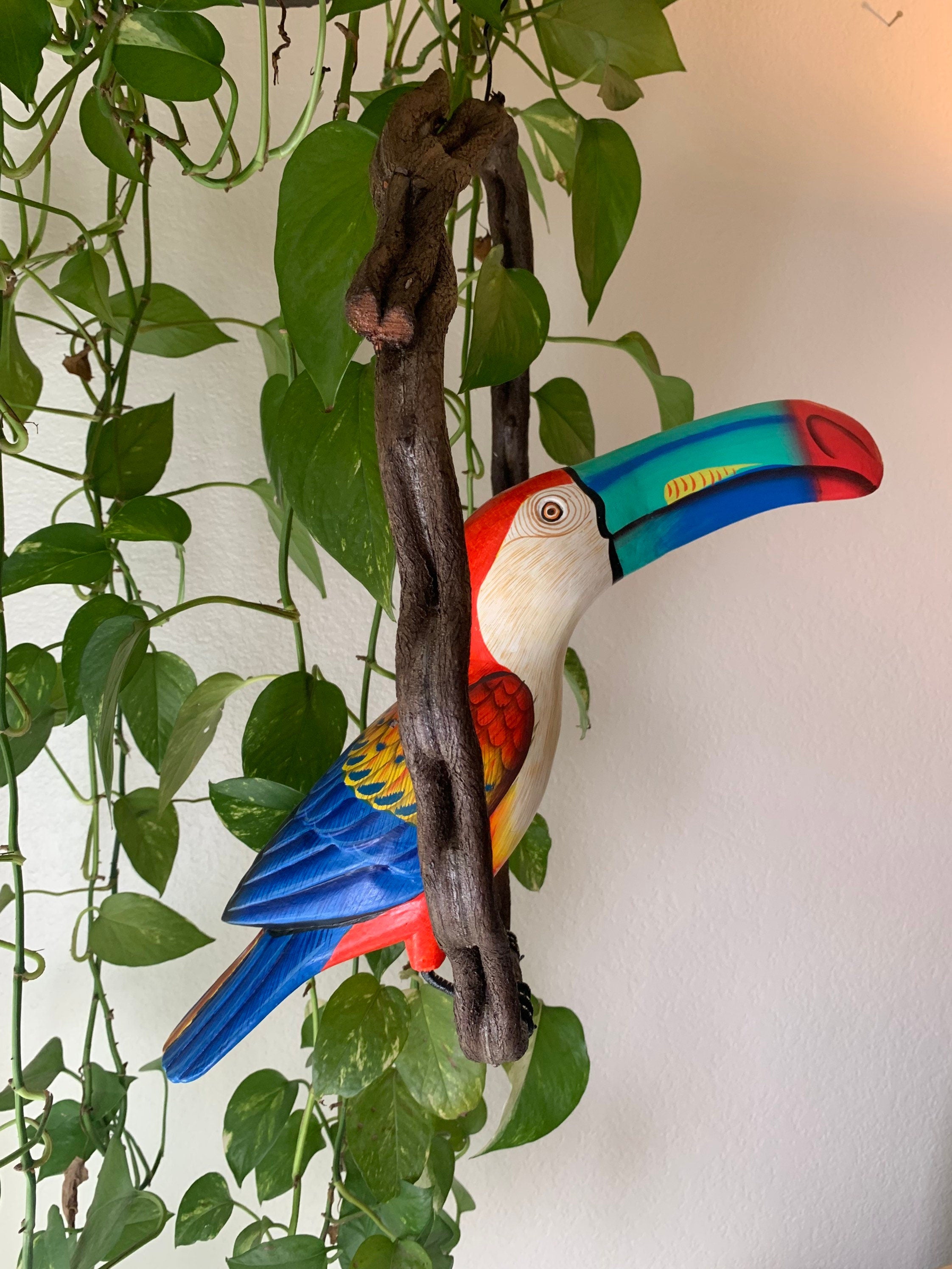 Colorful toucan sculpture perched on a branch among green climbing vines.