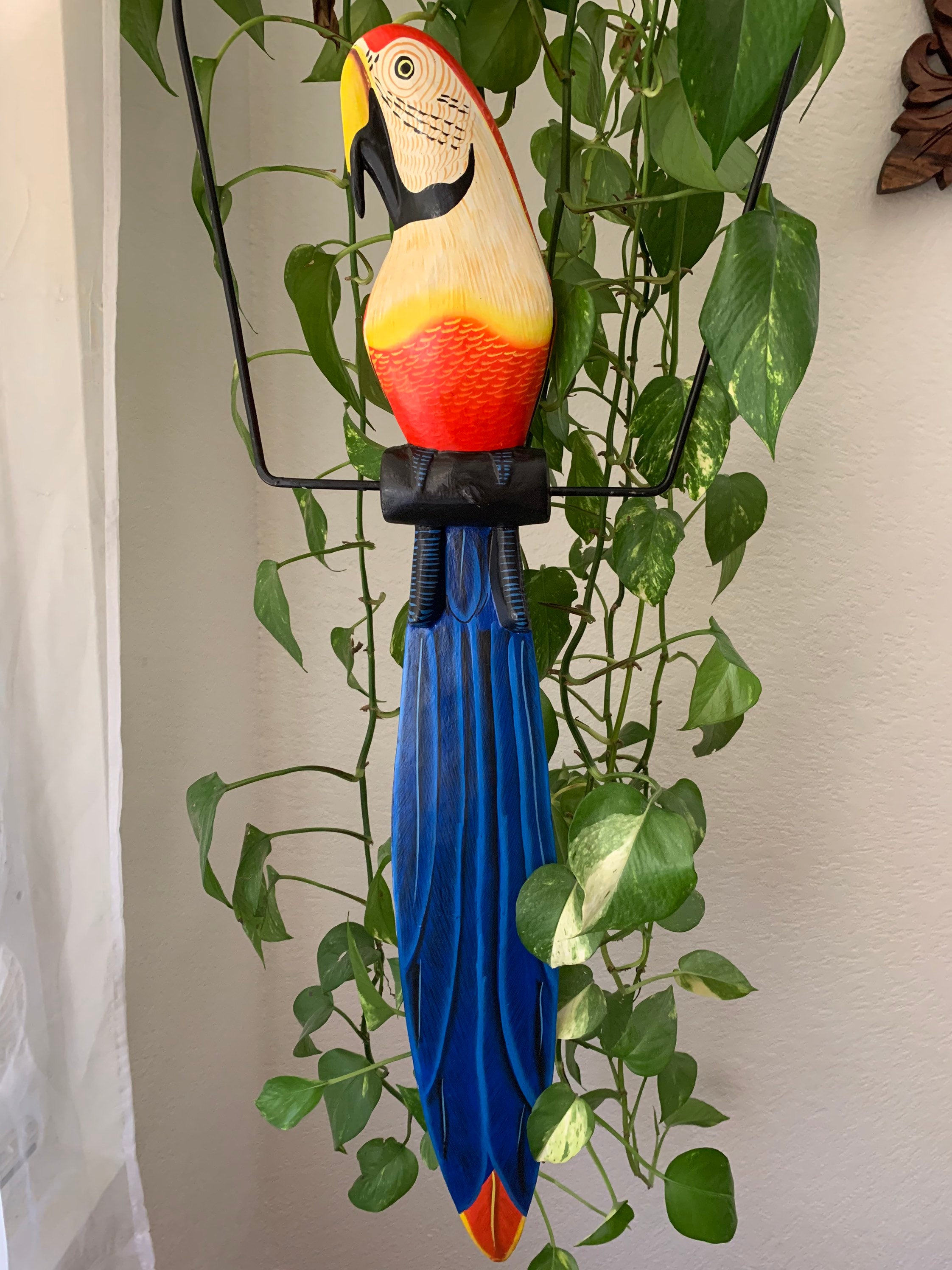 Colorful toucan sculpture with blue tail hanging among green pothos plants