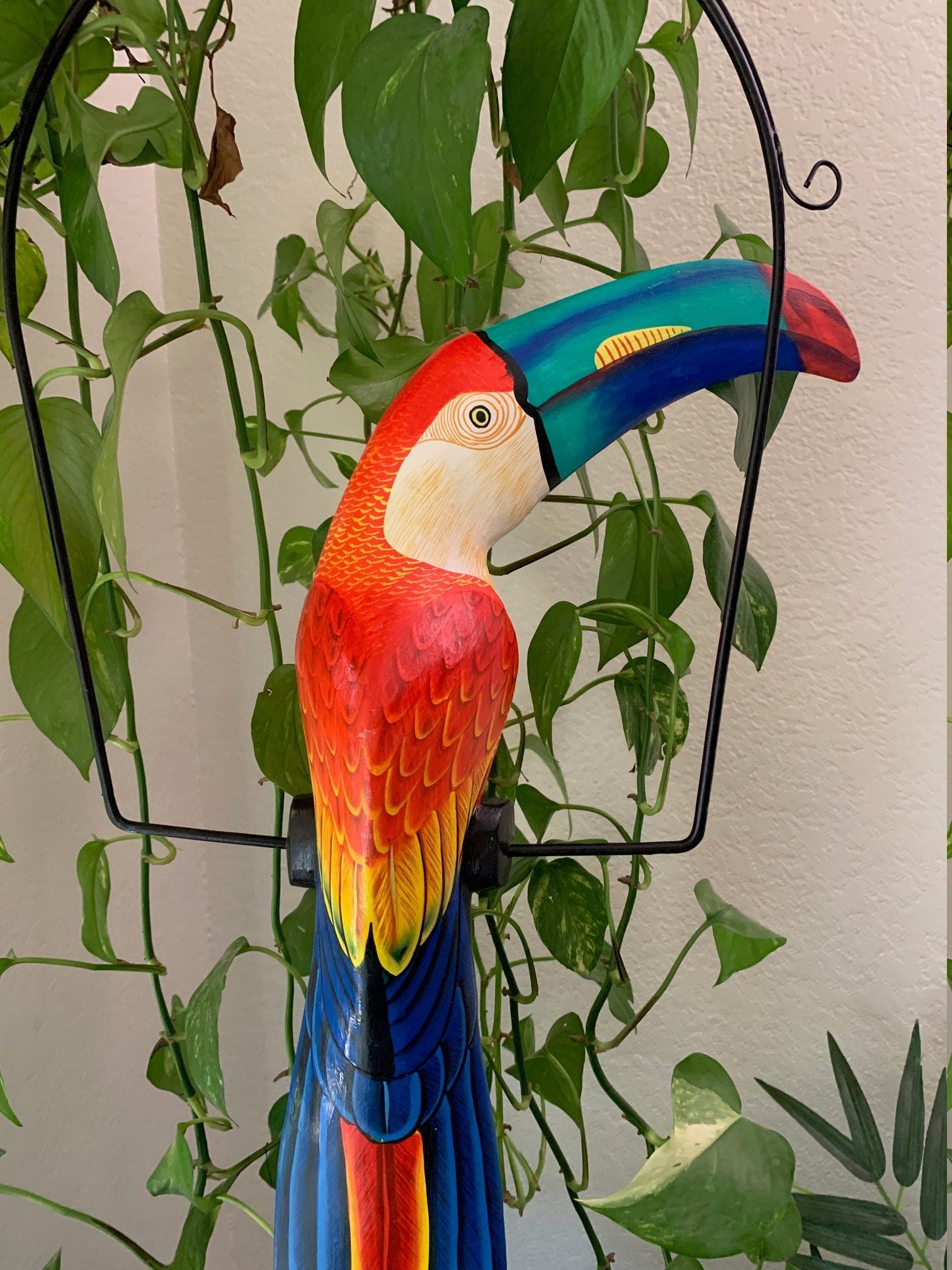 Colorful toucan sculpture with a bright rainbow beak among green leafy plants.