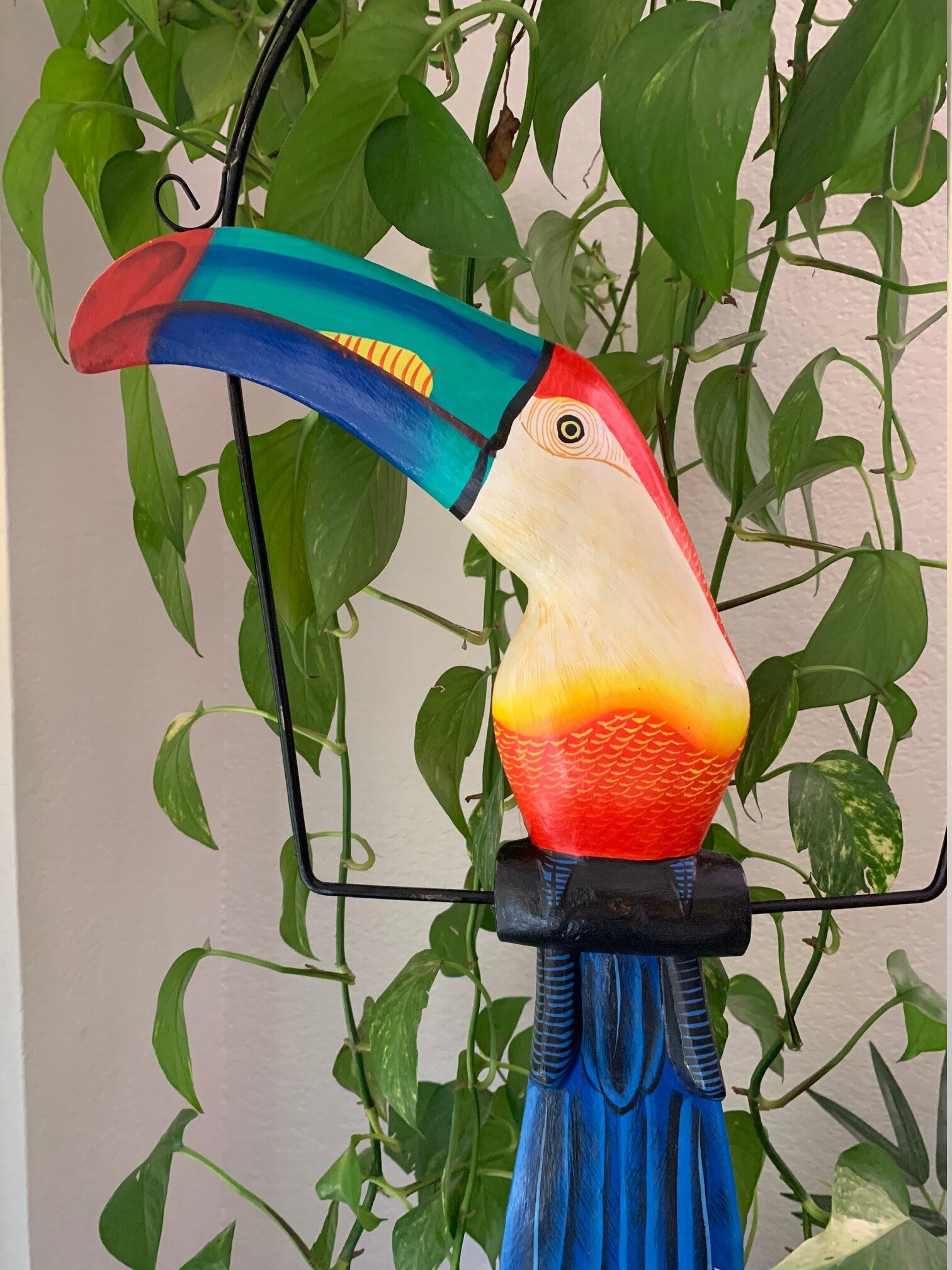 Colorful toucan sculpture with rainbow beak and blue body among green plants