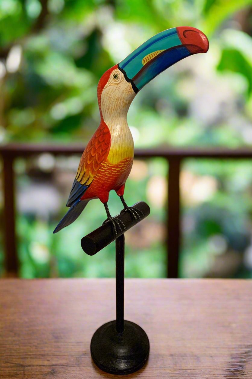 Colorful wooden toucan statue perched on a black stand outdoors.