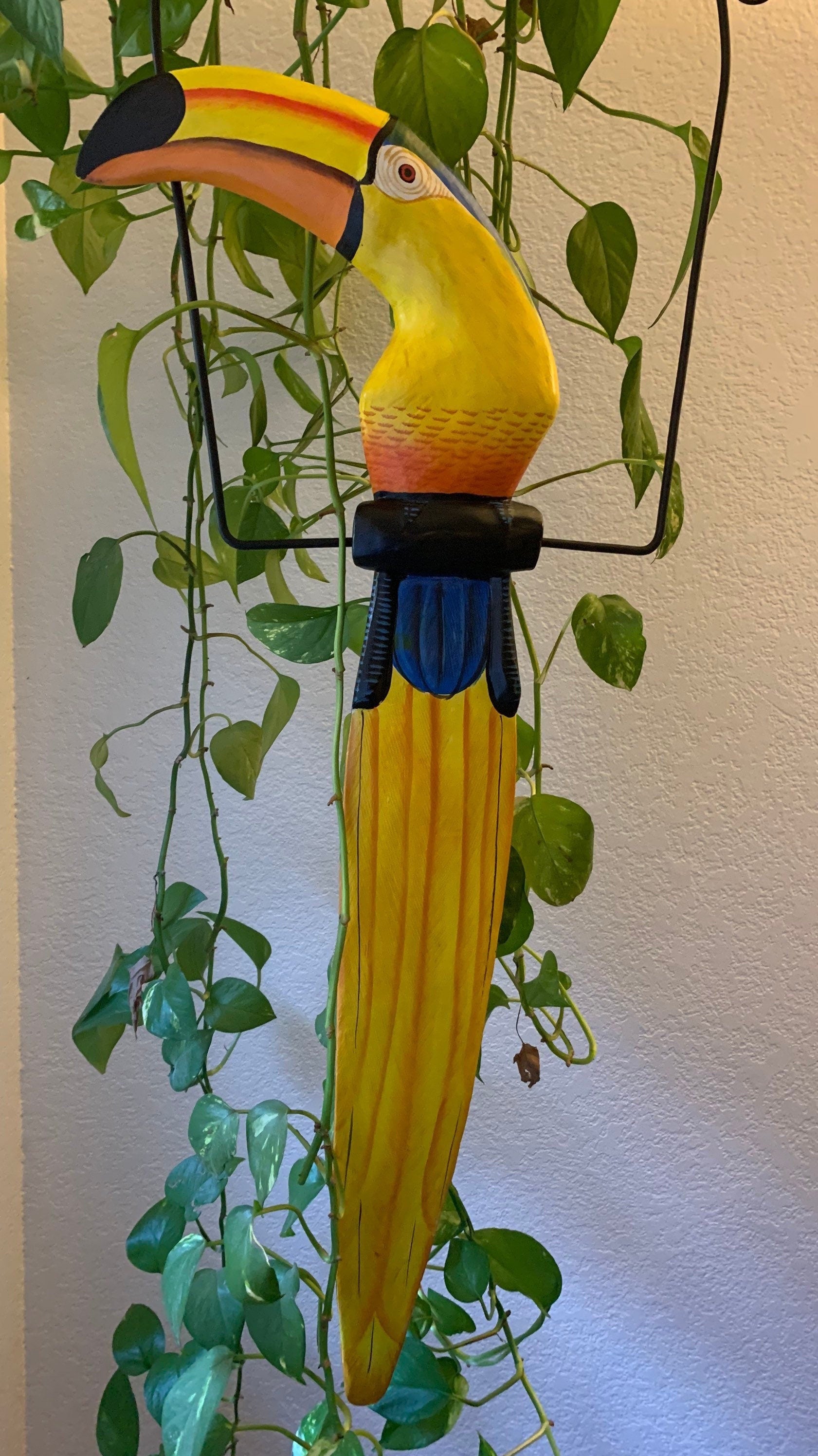 Colorful wooden toucan sculpture hanging among green plants