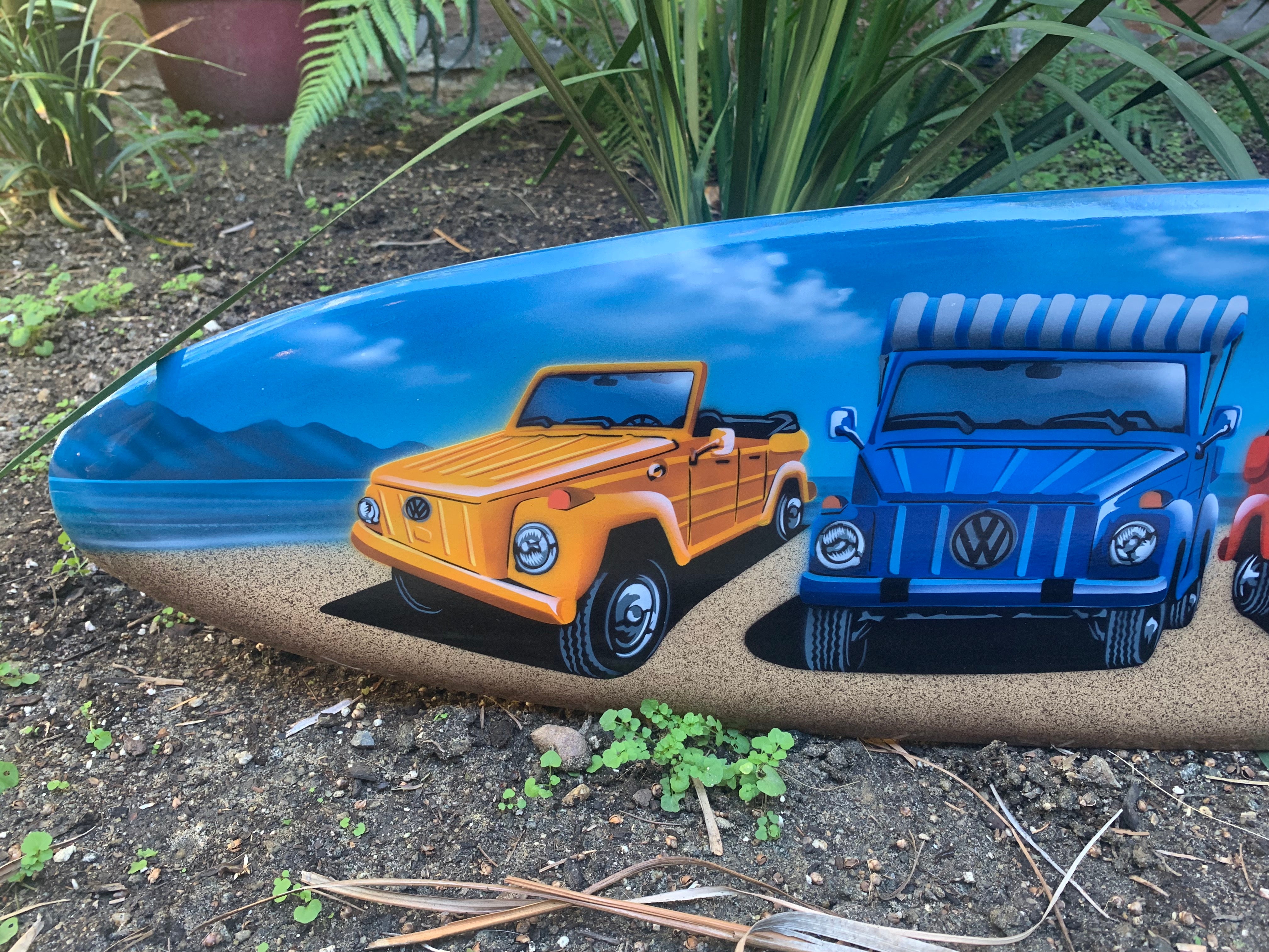 Colorful VW vans painted on a beach scene with water and mountains in the background