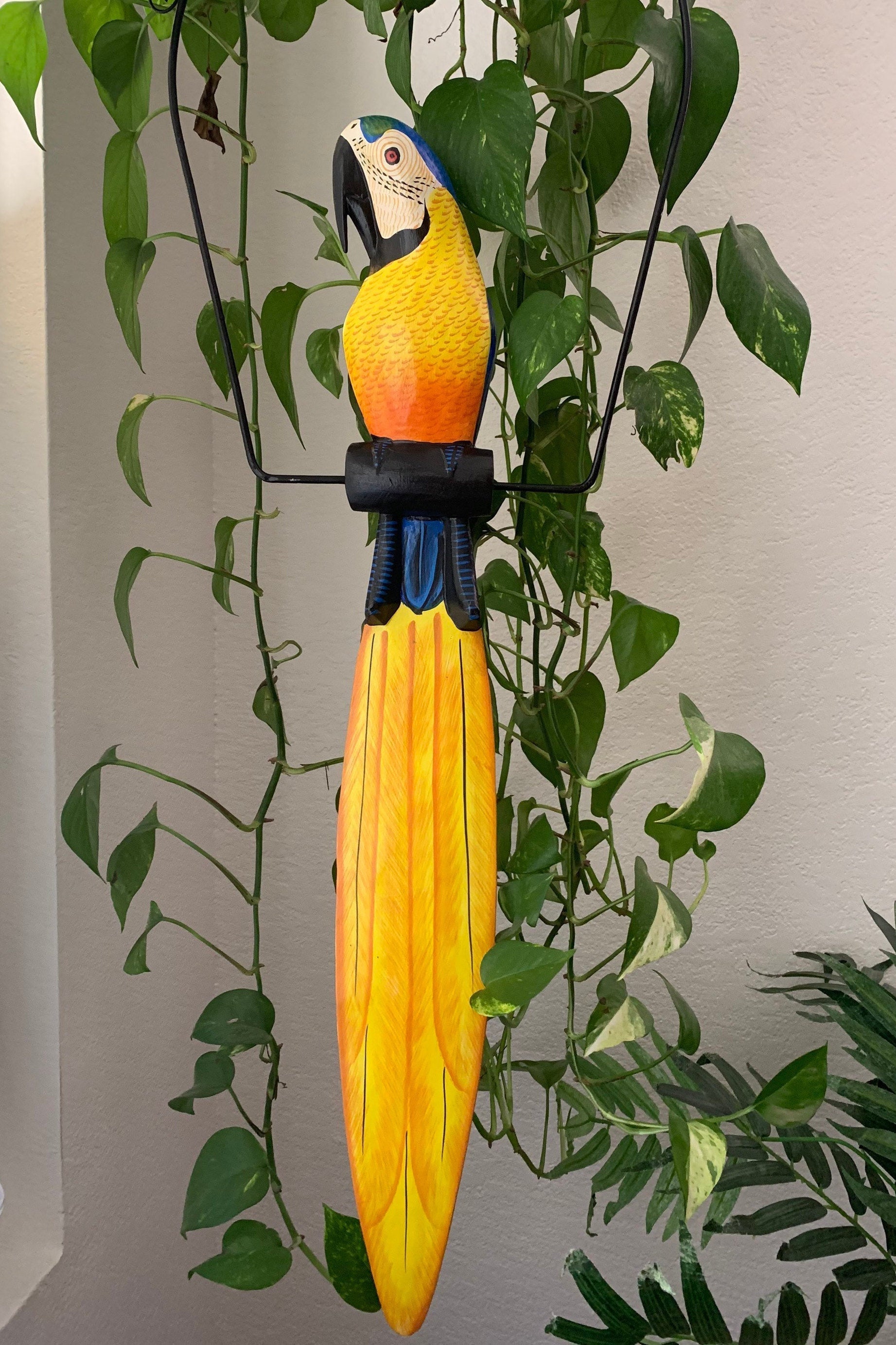 Colorful wooden parrot sculpture with long yellow tail among green plants