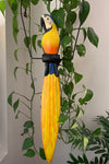 Colorful wooden parrot sculpture with long yellow tail among green plants