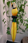 Colorful wooden parrot sculpture with long yellow tail among green houseplants