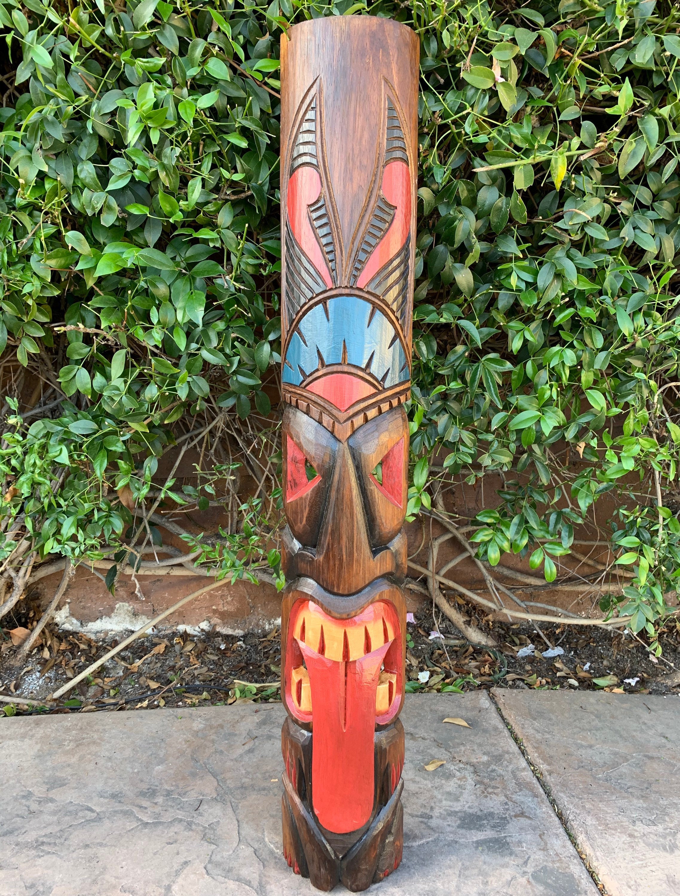 Colorful wooden tiki totem pole with red, blue, and brown carvings outdoors.