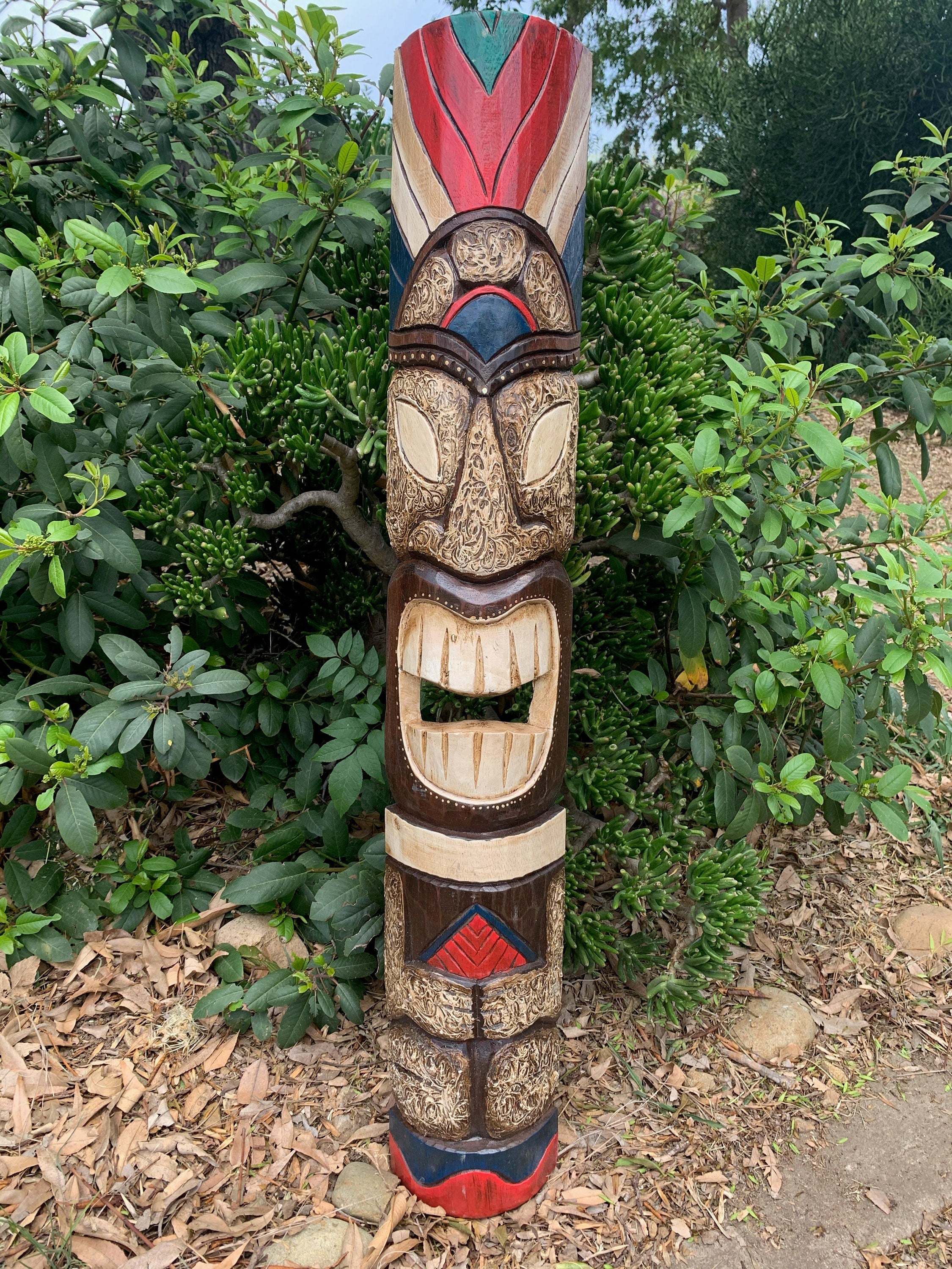 colorful carved tiki totem pole with an open mouth, outdoors among green shrubs