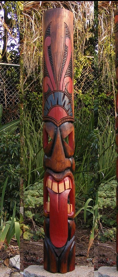 Colorful wooden totem pole carving with geometric shapes in a garden setting.