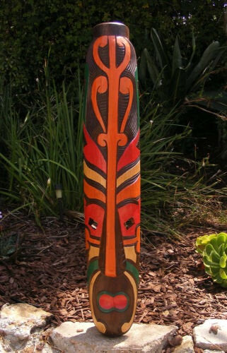 Colorful wooden totem pole with red and orange tribal patterns in a garden.