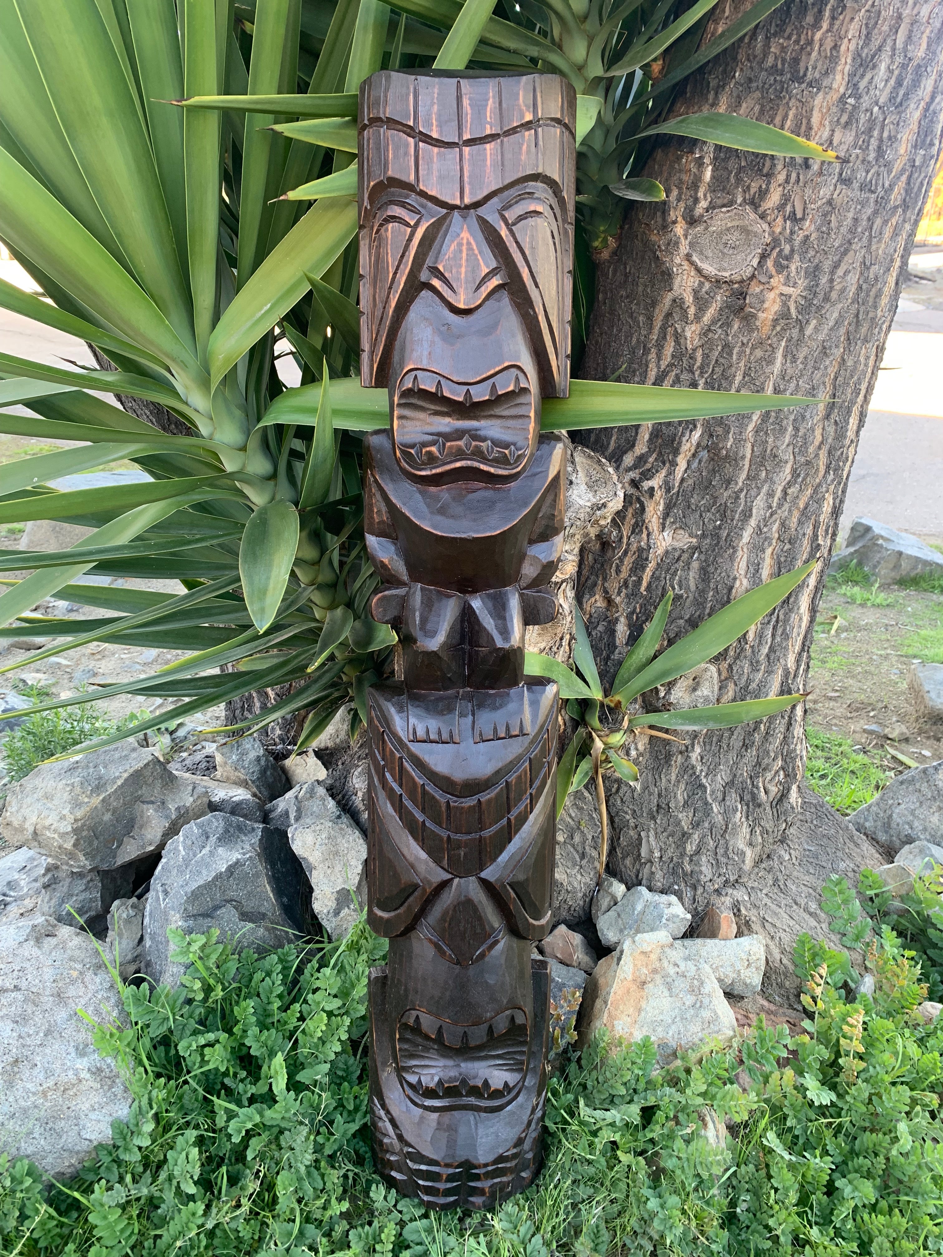 Dark wood tiki totem carving mounted on a tree in an outdoor garden