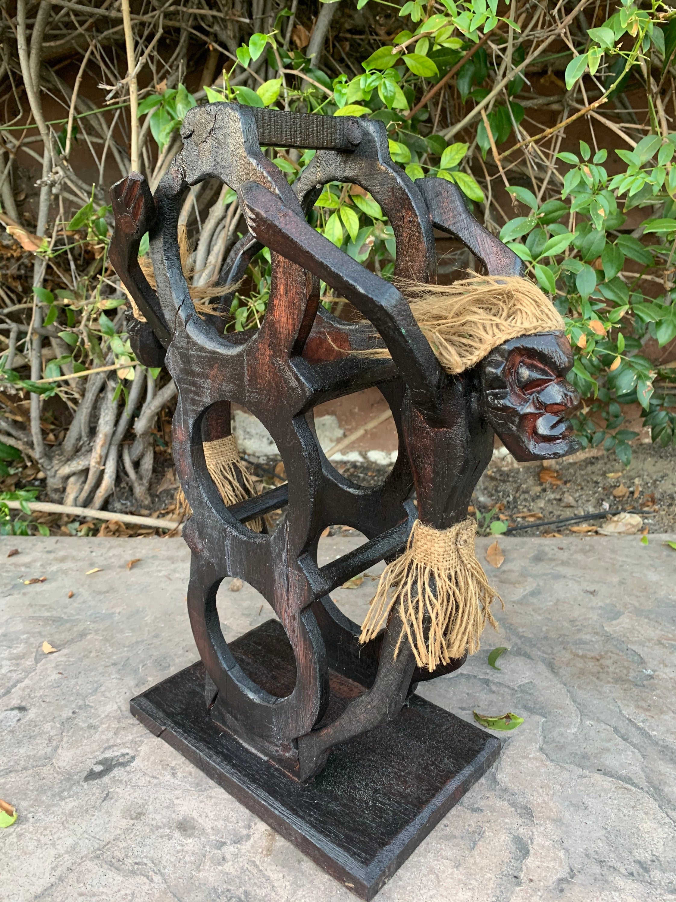 Dark wooden abstract sculpture with circular cutouts and rope tassels outdoors