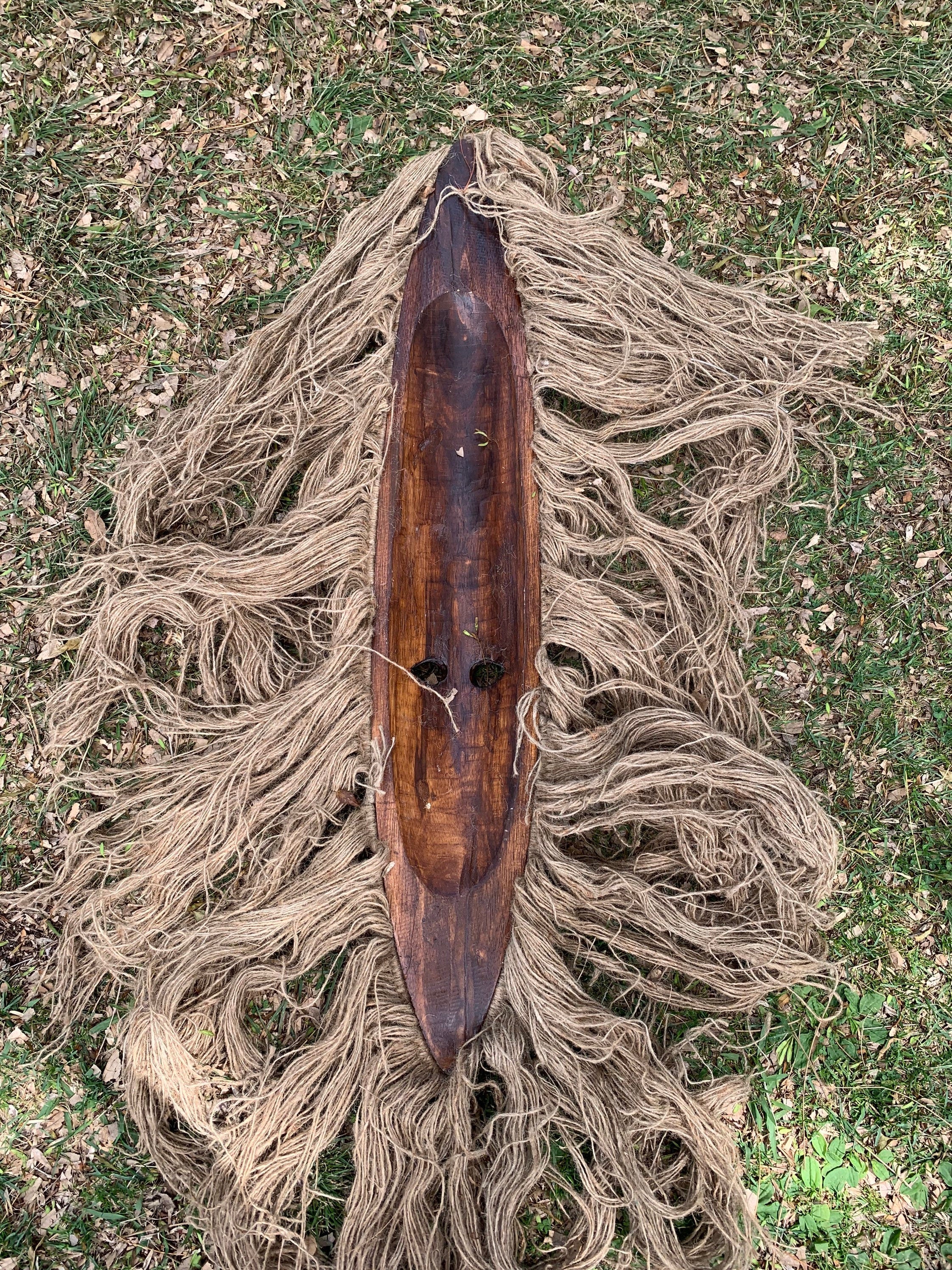 Dark wooden canoe-shaped object on grass with tangled natural fiber rope