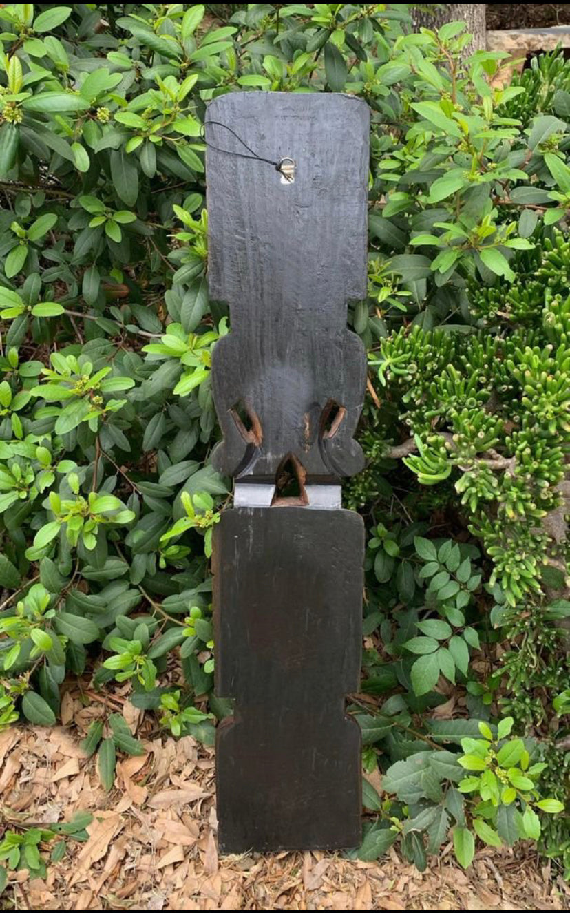 Dark wooden totem-style sculpture in a garden among green shrubs