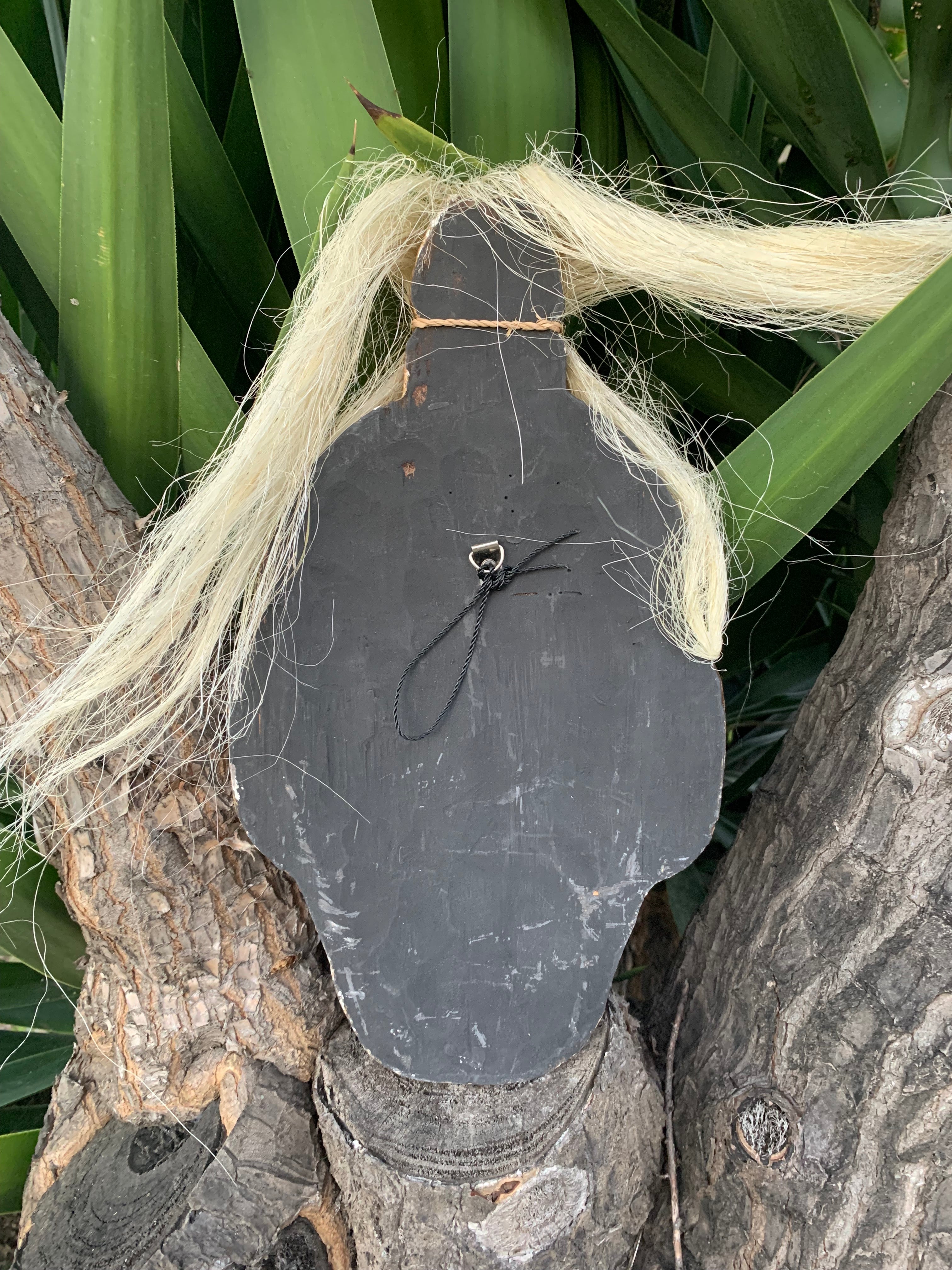 Dark wooden silhouette in the shape of a person with a long blonde wig mounted on a tree trunk