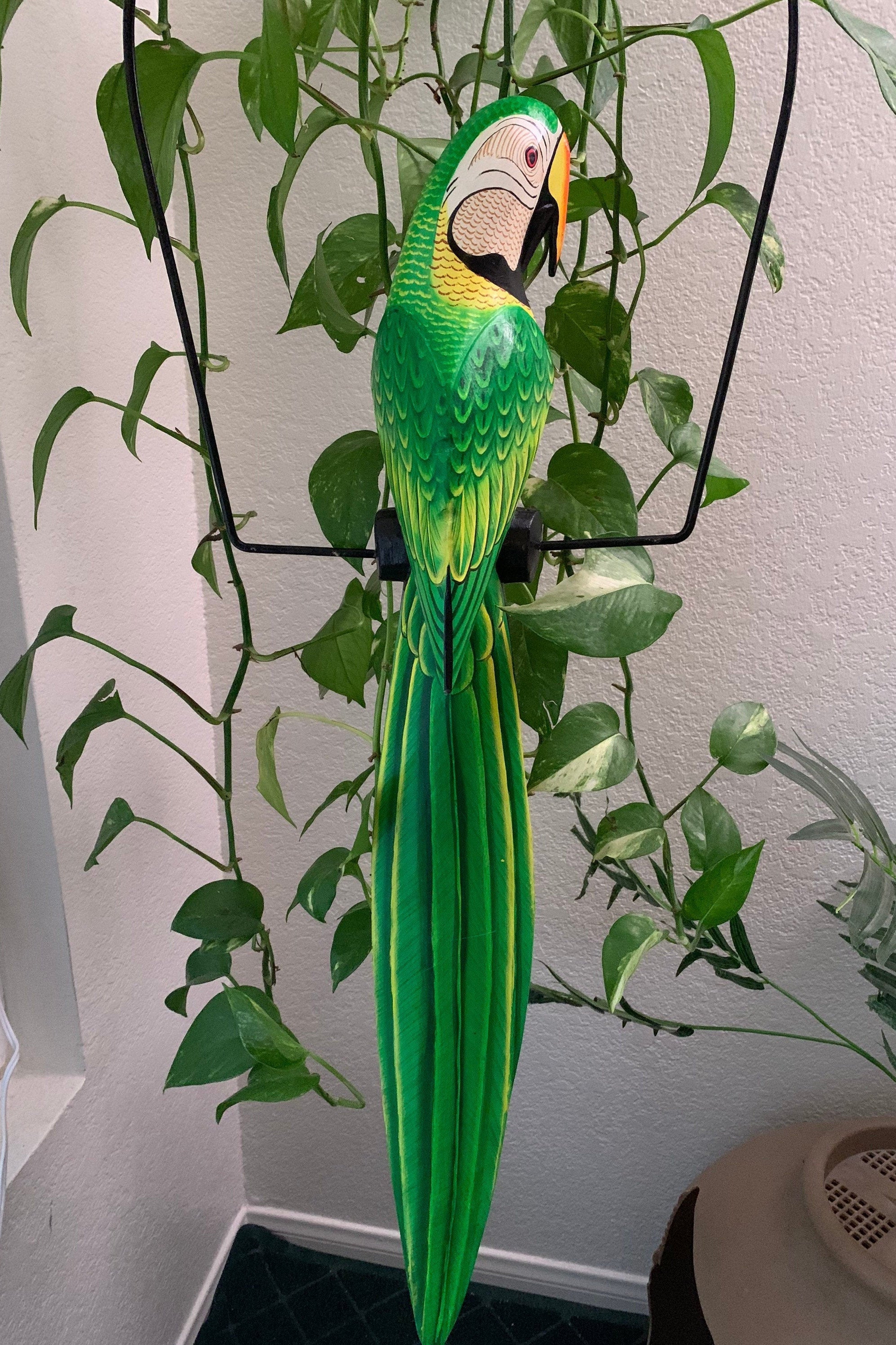 Decorative green macaw parrot sculpture perched among trailing houseplants