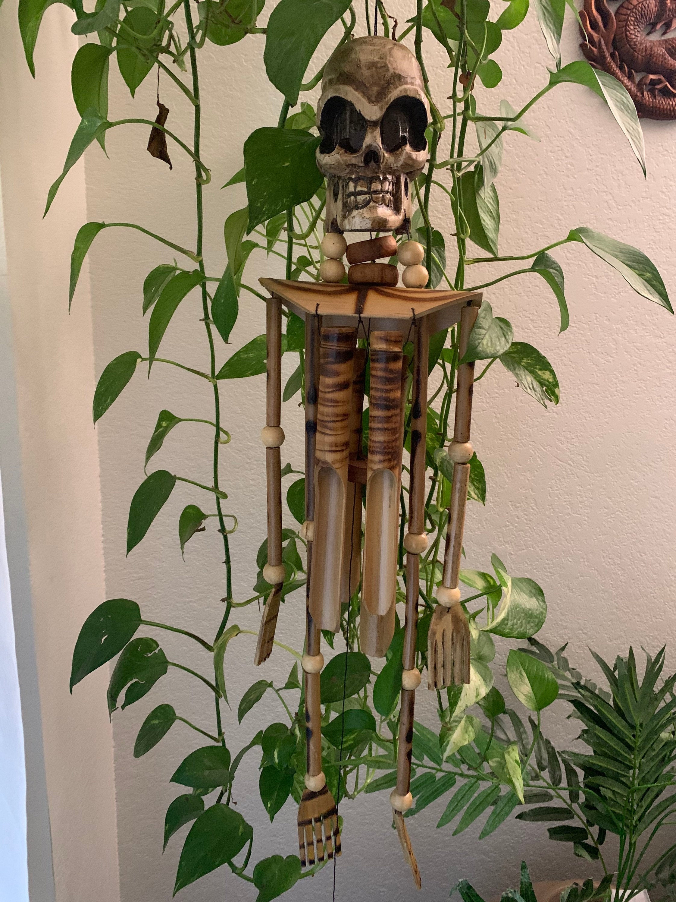 Decorative skull wind chime with wooden beads hanging among green plants.