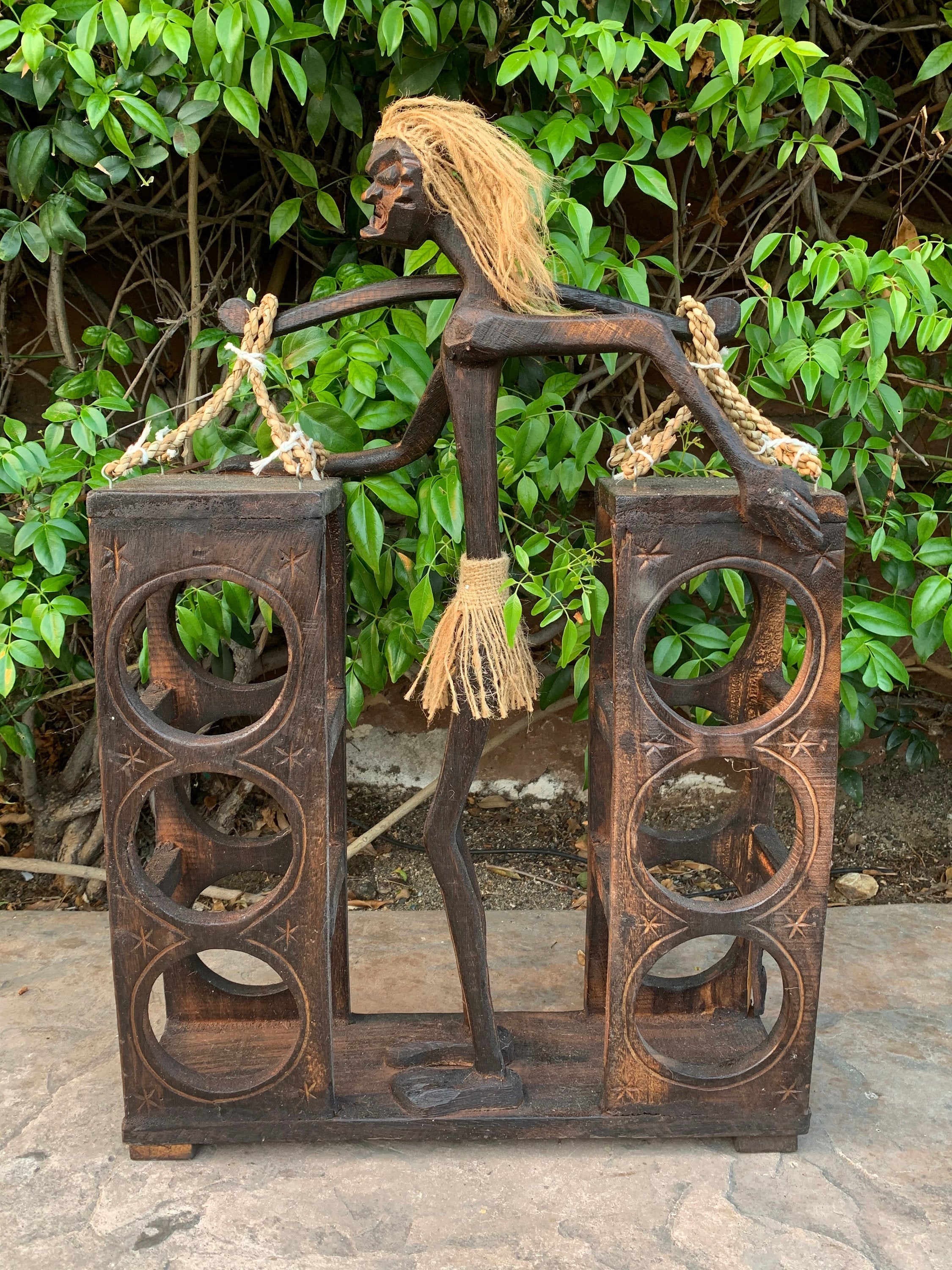 Rustic carved wooden figure balancing two rope-handled boxes with circular cutouts