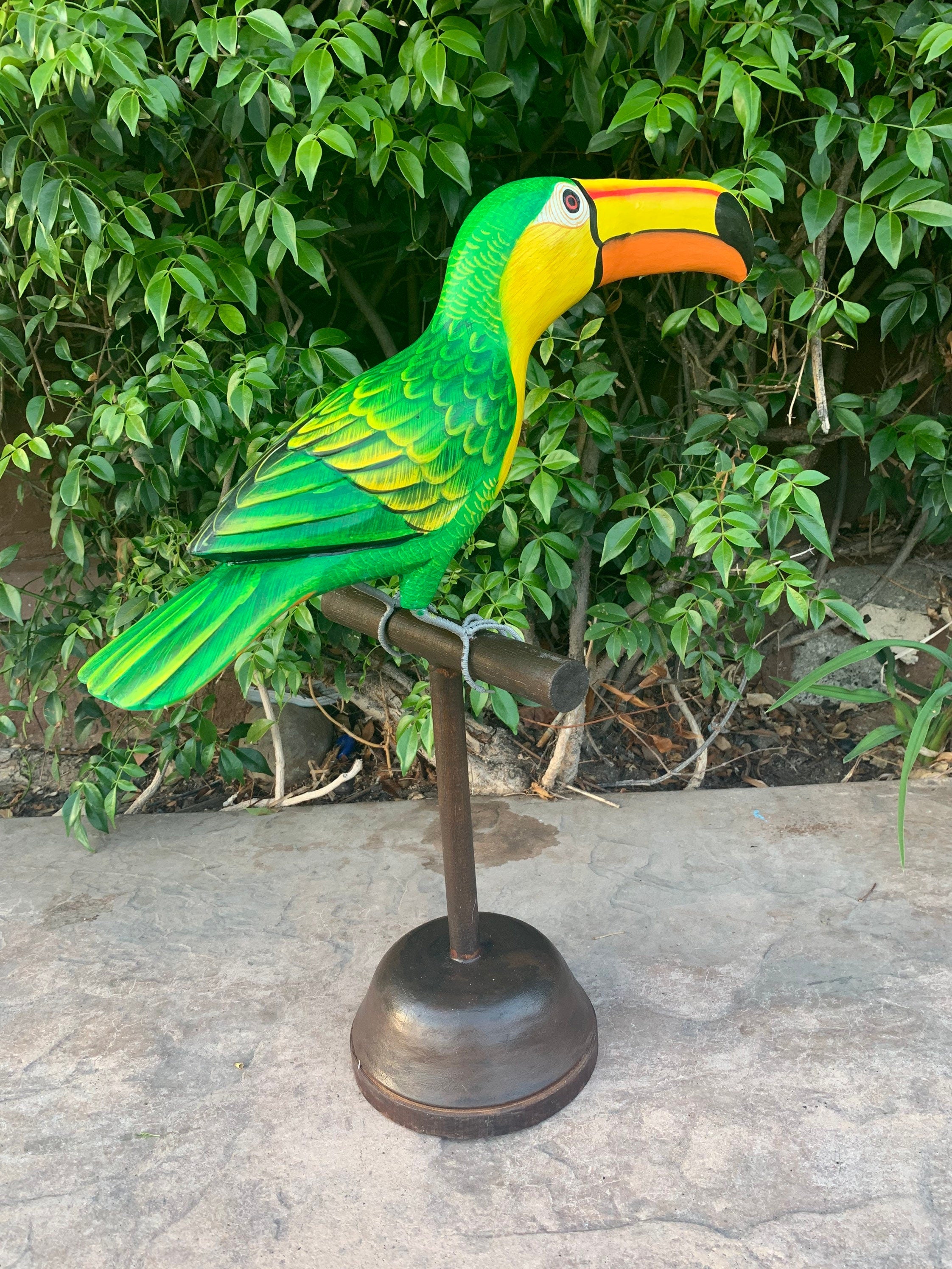 Colorful green parrot sculpture perched on a metal stand in a garden