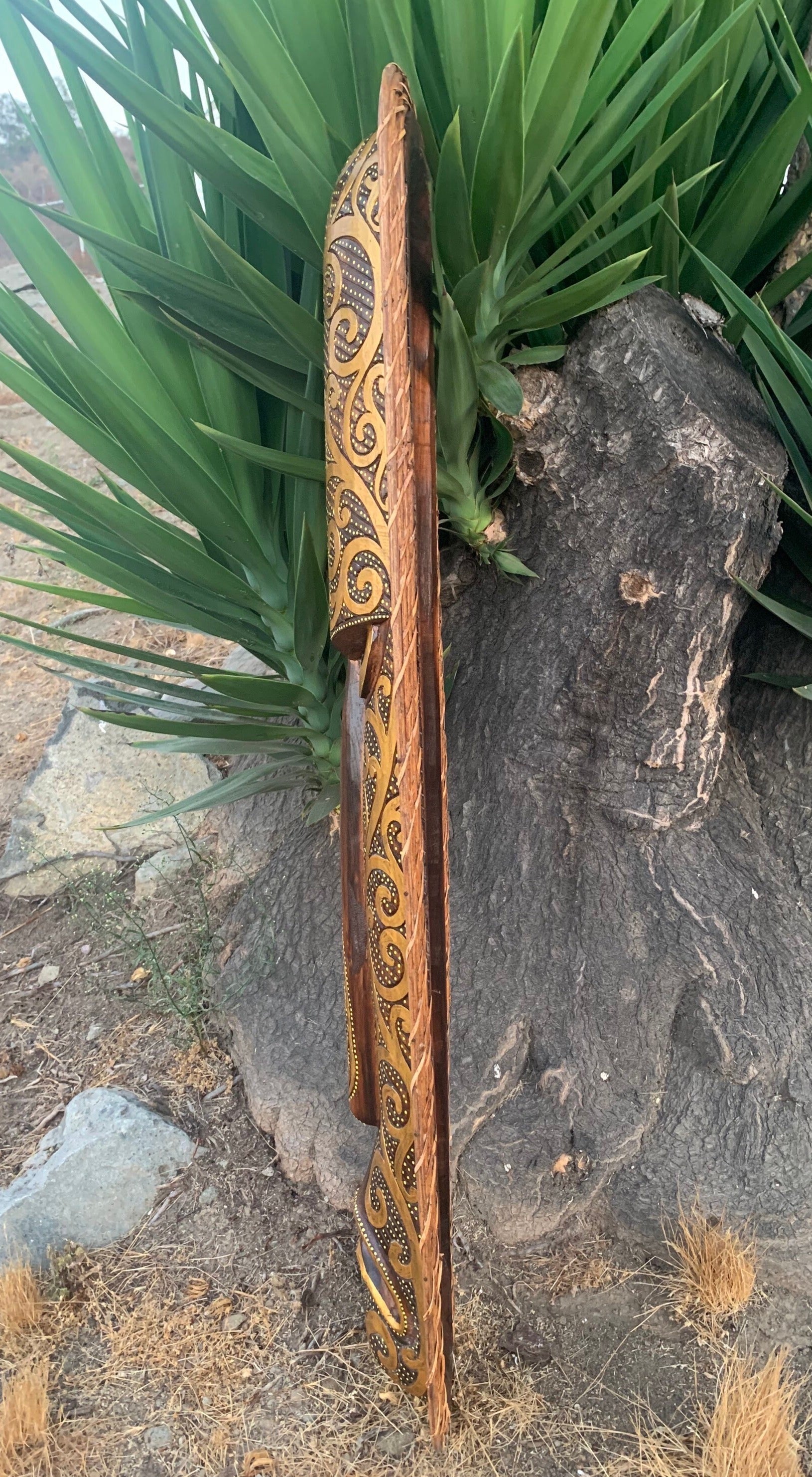 Hand-carved wooden staff with gold swirl pattern leaning against a tree beside green plants
