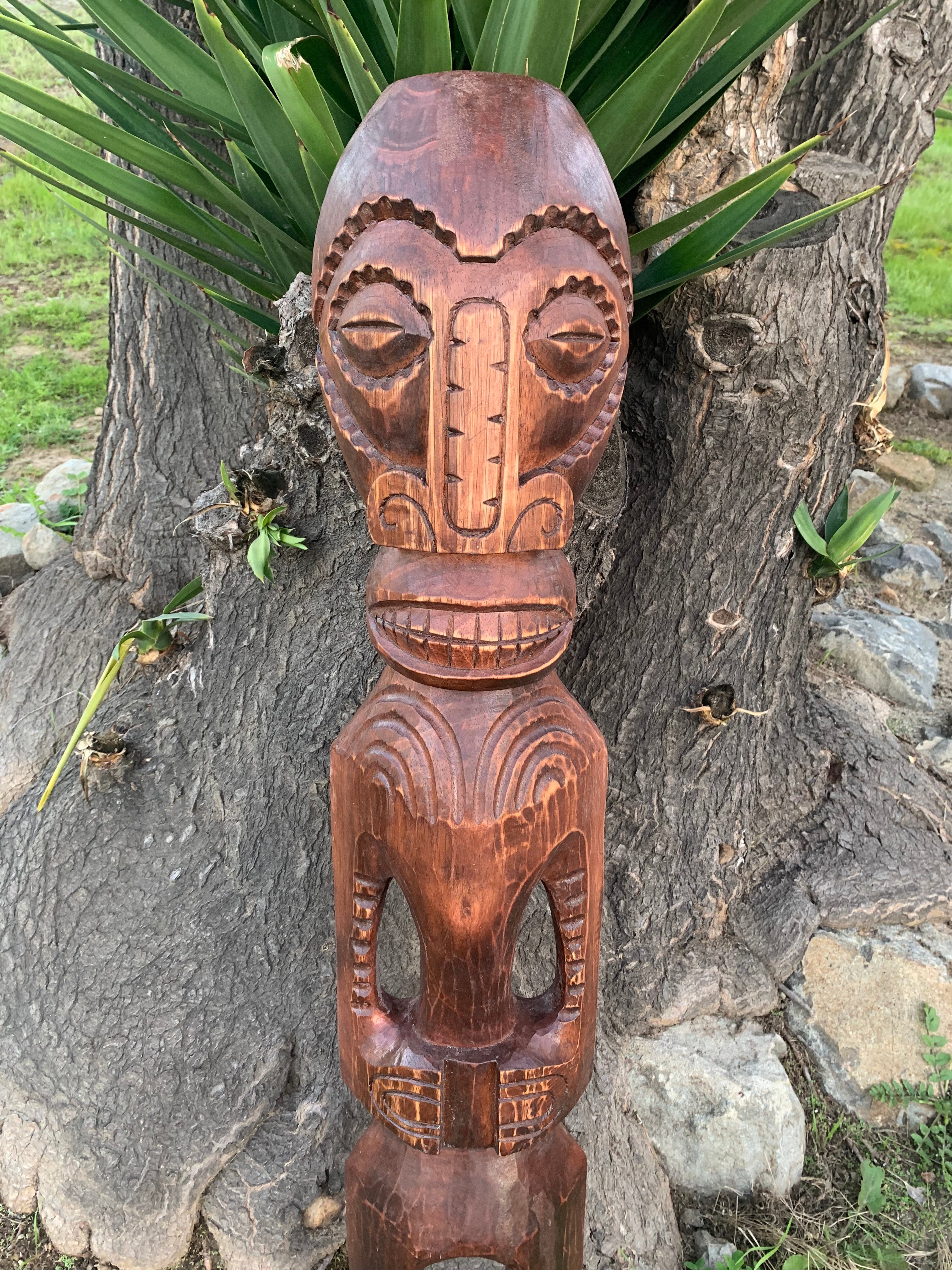 Hand-carved wooden tiki mask sculpture mounted on a tree trunk outdoors.