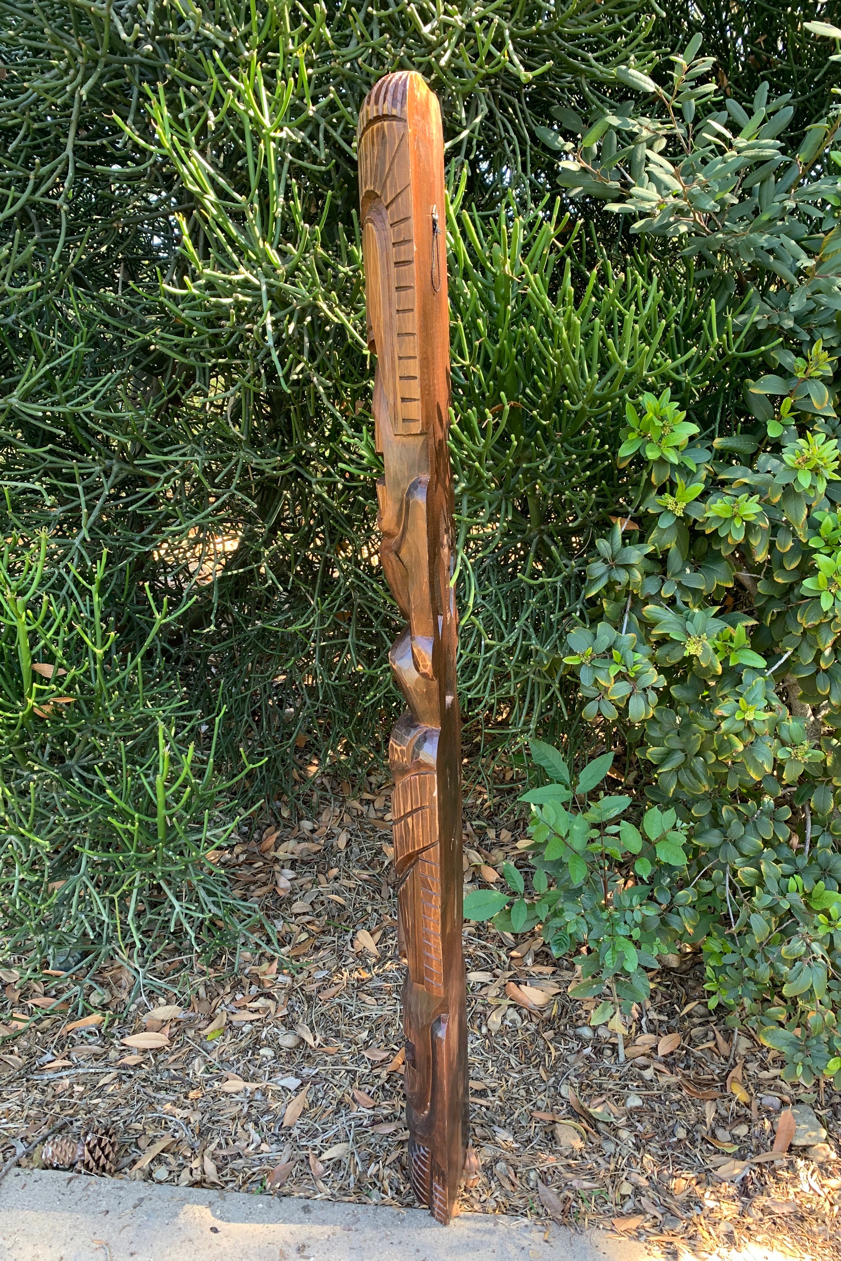 Hand-carved wooden totem pole standing in a garden among green shrubs