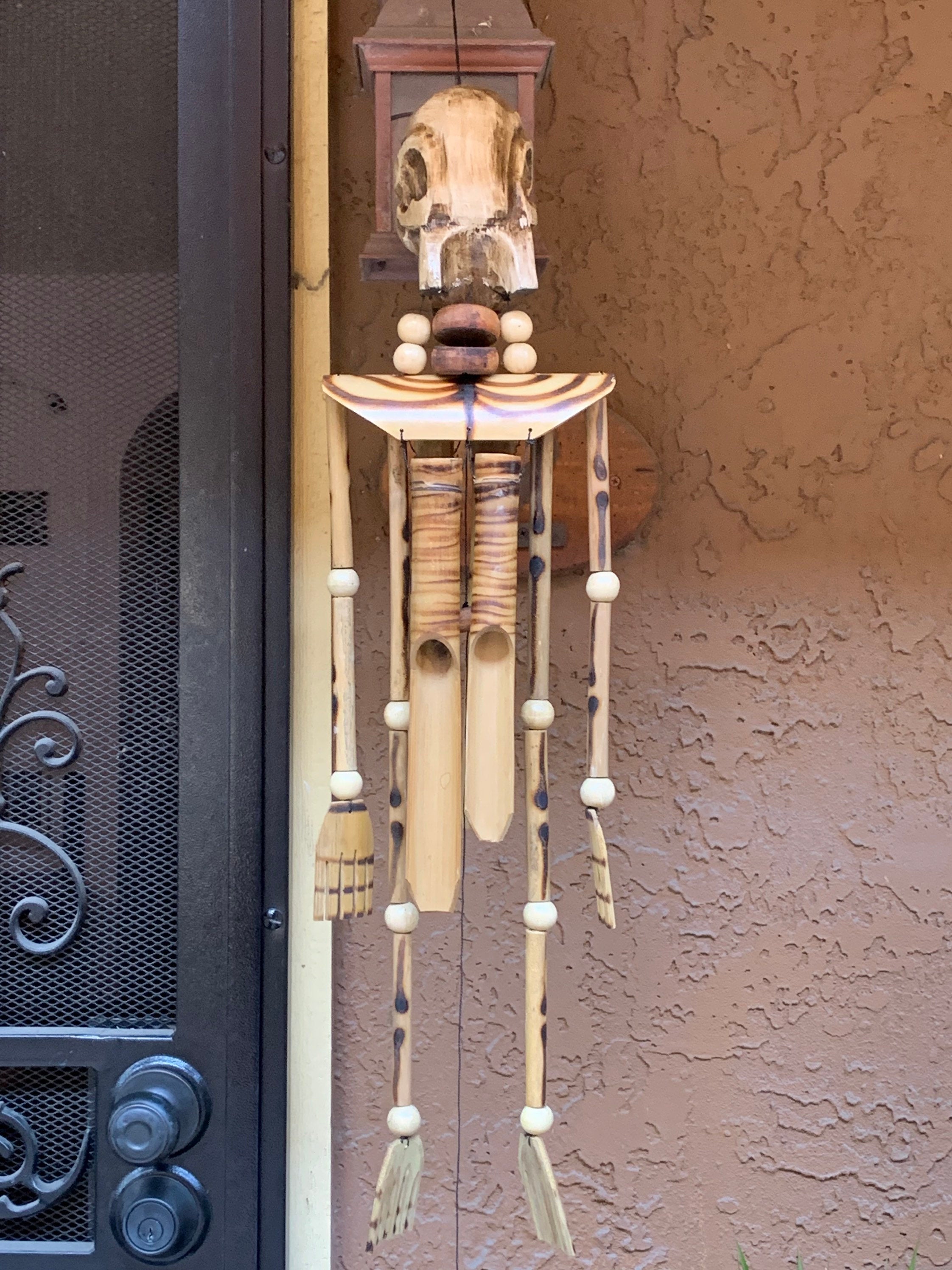 handmade wooden skeleton wind chime hanging sculpture on stucco wall
