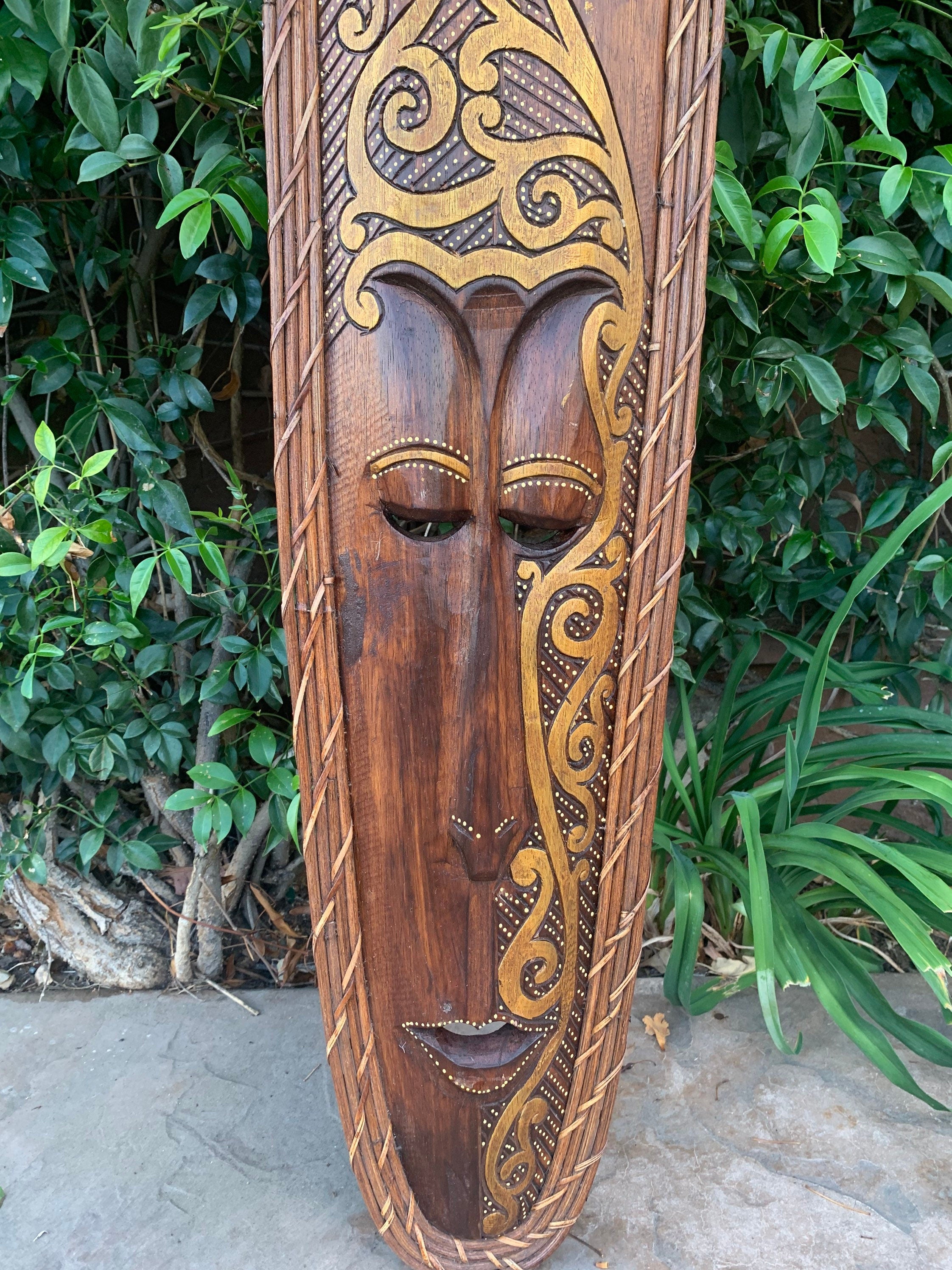 intricately carved wooden tribal mask with gold embellishments displayed outdoors
