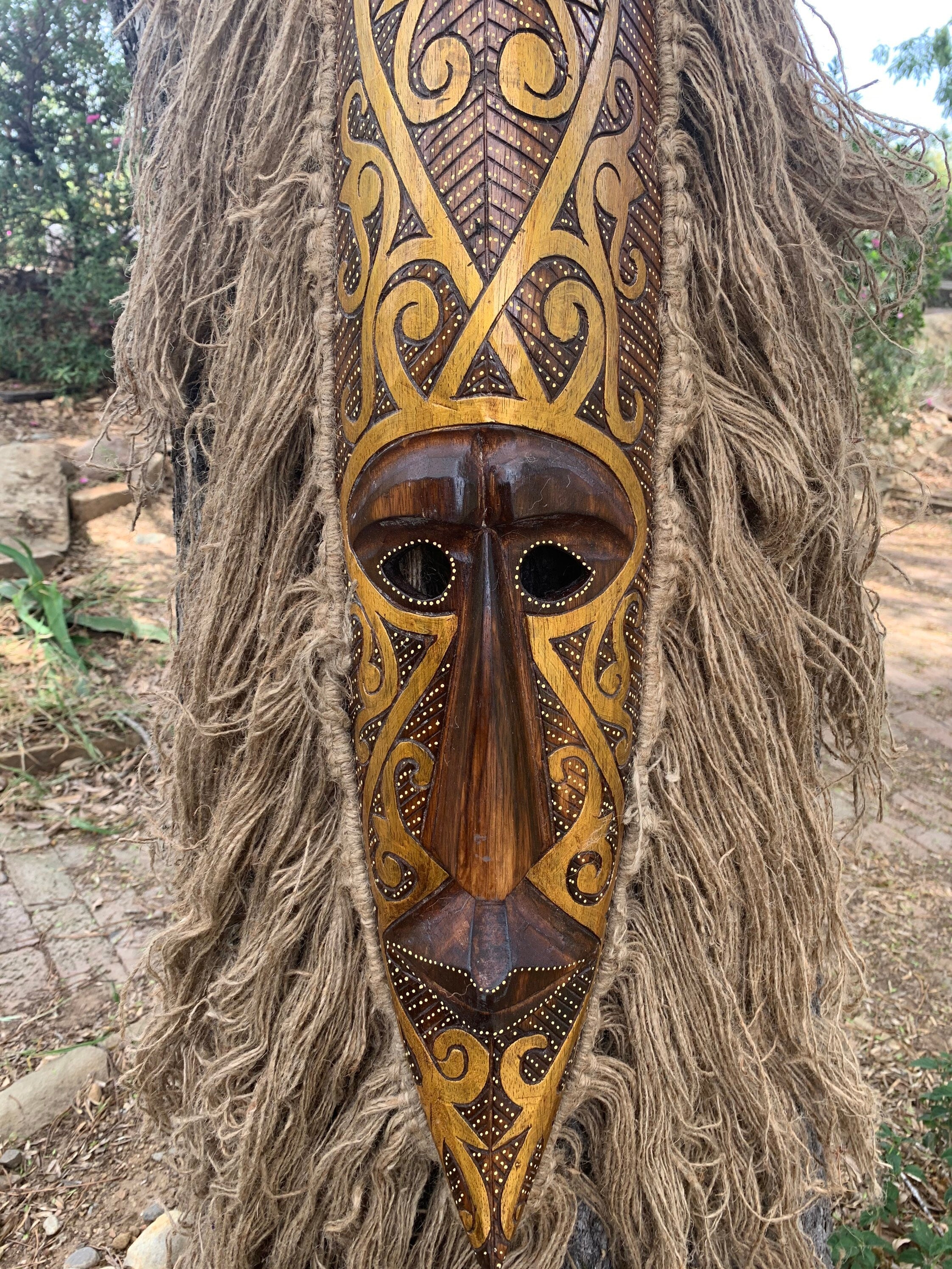 Intricately carved wooden mask with gold patterns hanging on a tree