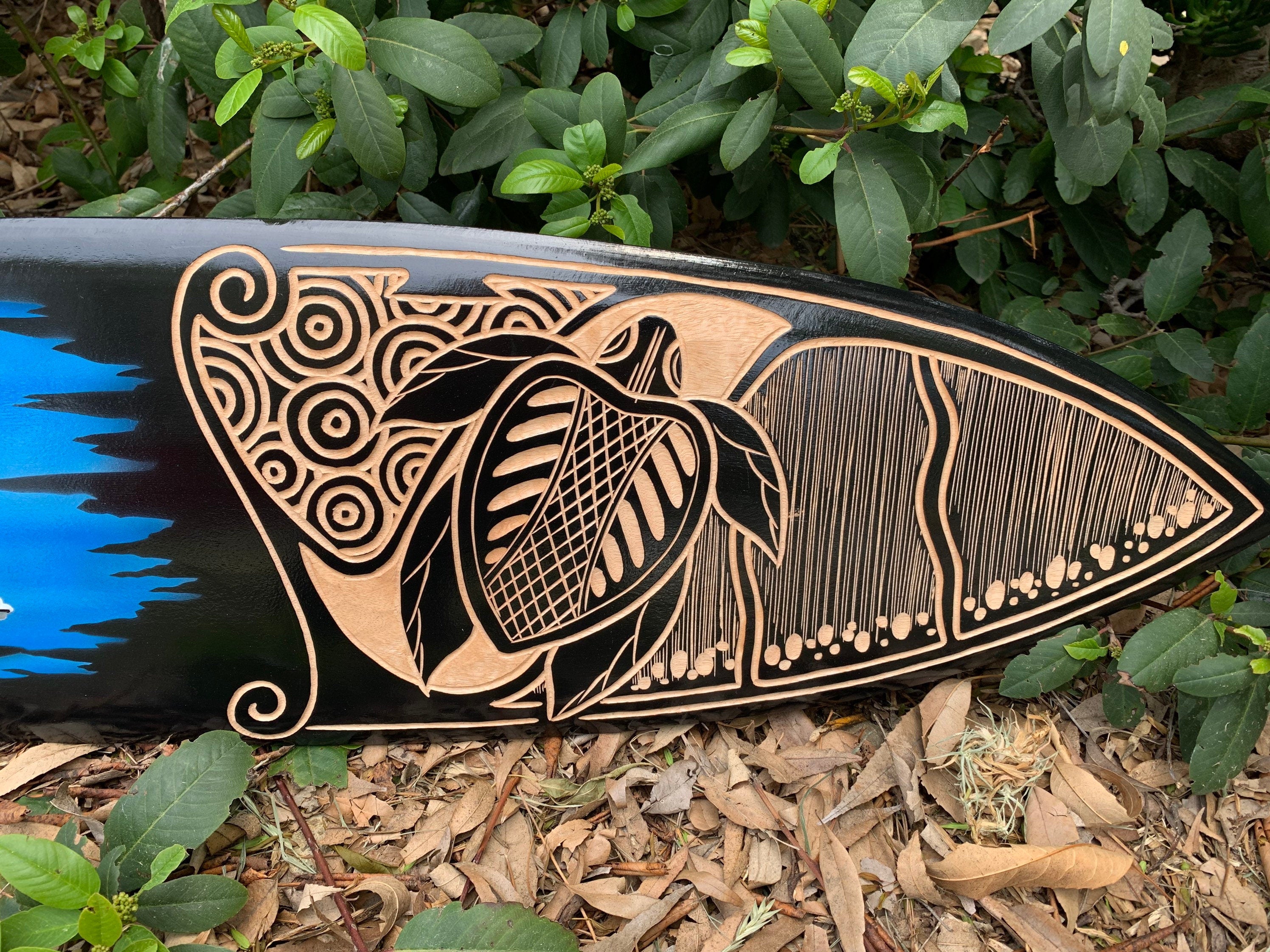 Maori-inspired wood-carved surfboard featuring spirals and a bird motif on a black background