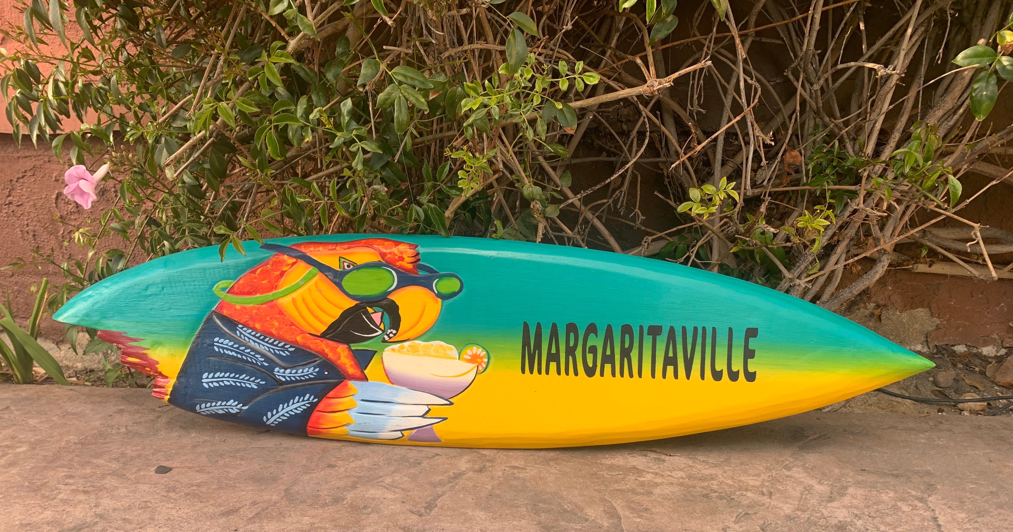 colorful Margaritaville surfboard with tropical gradient colors leaning against a bush