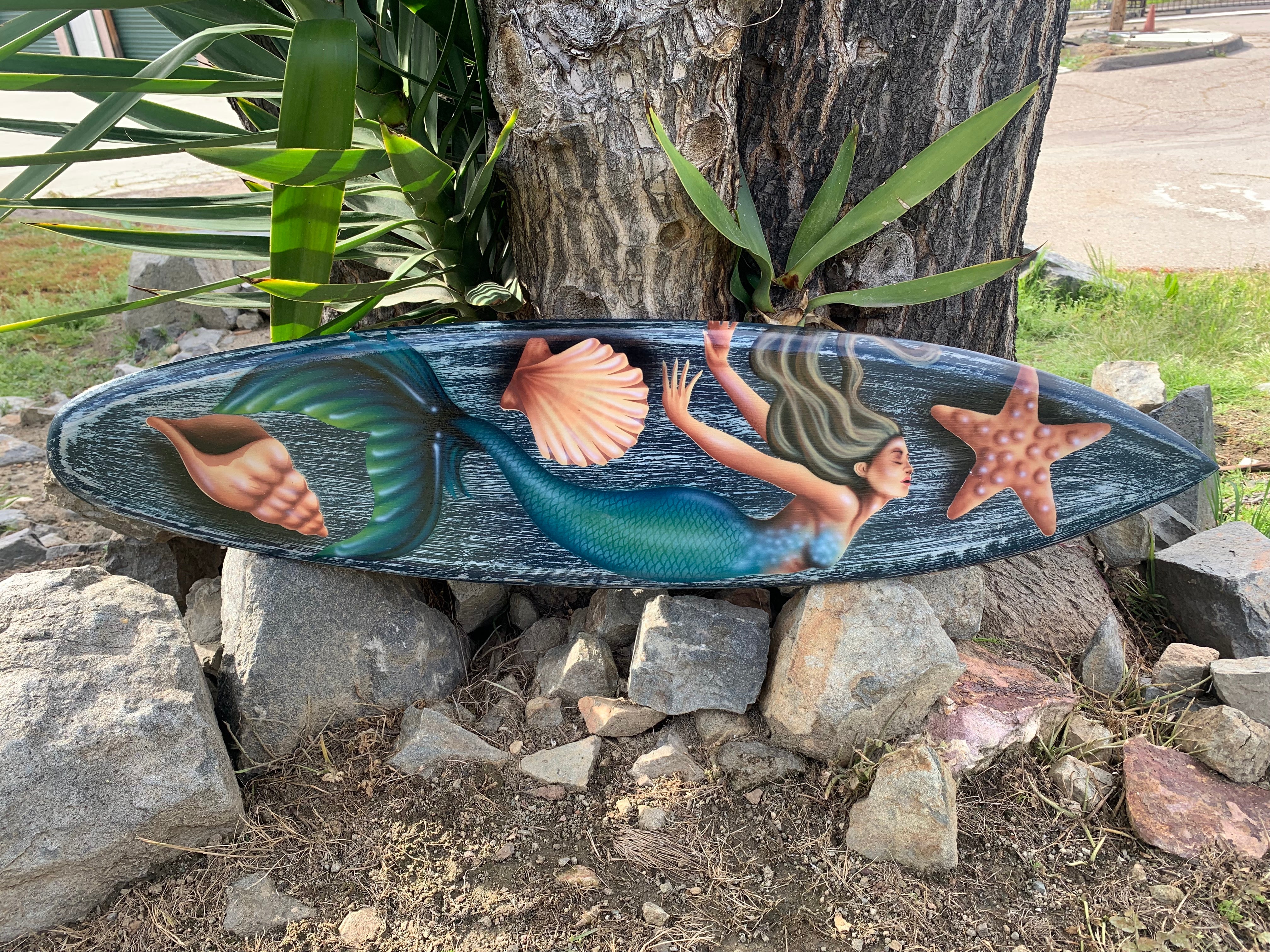 Mermaid on blue surfboard with seashells and a starfish