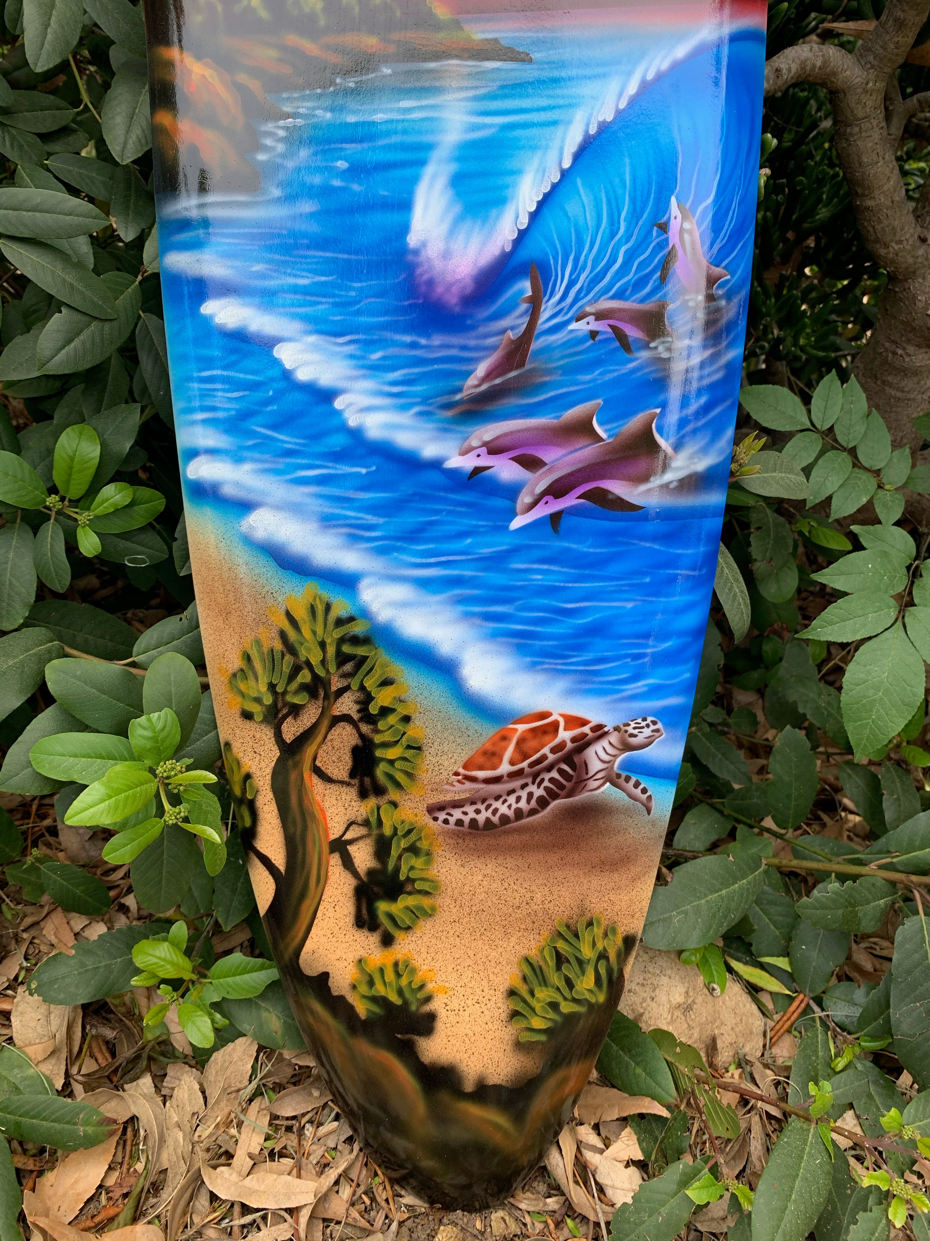 Tall outdoor sculpture painted with an ocean scene featuring dolphins, waves, sandy beach, and a sea turtle.