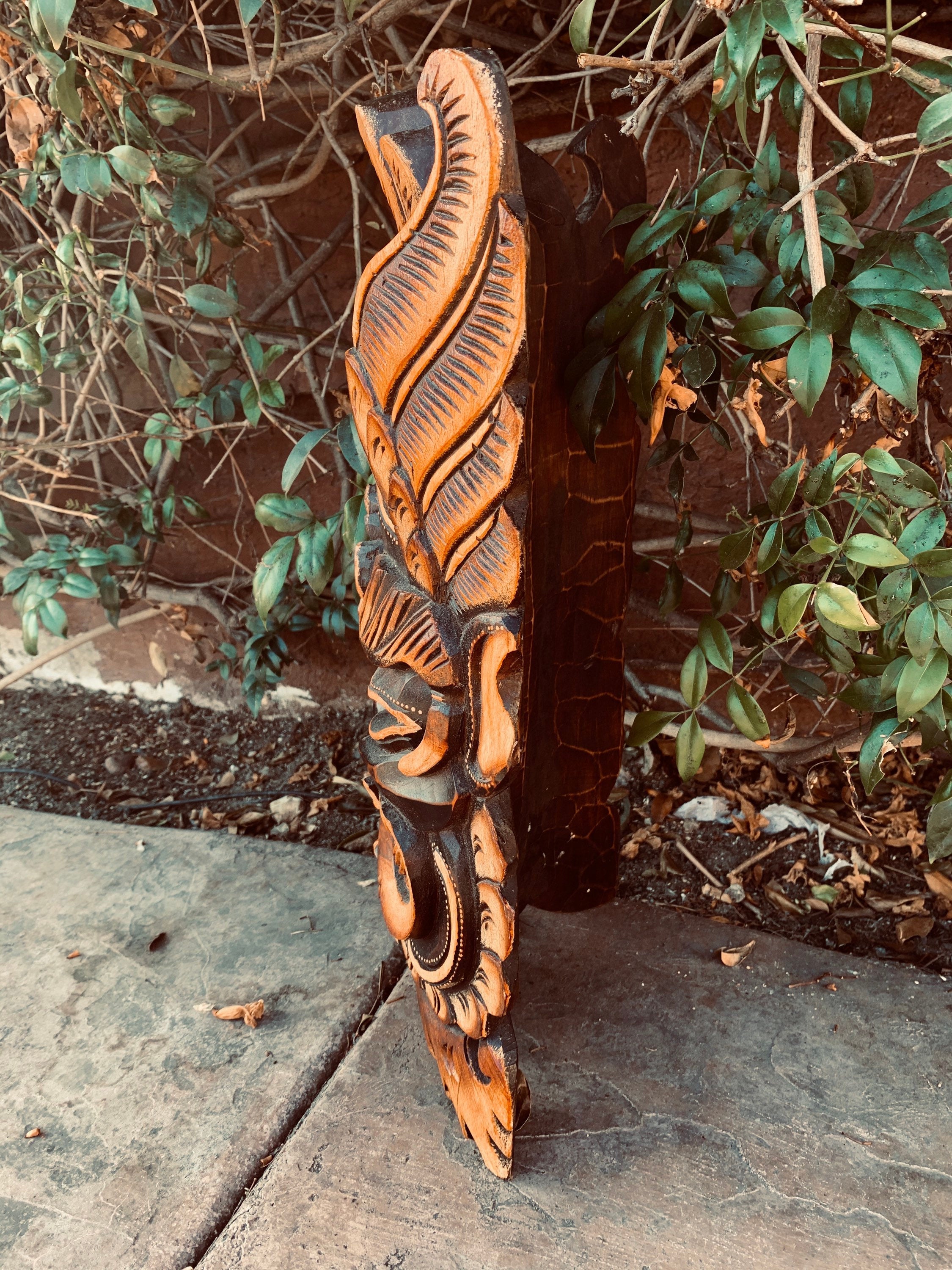 Orange and black carved wooden totem in a garden with green vines