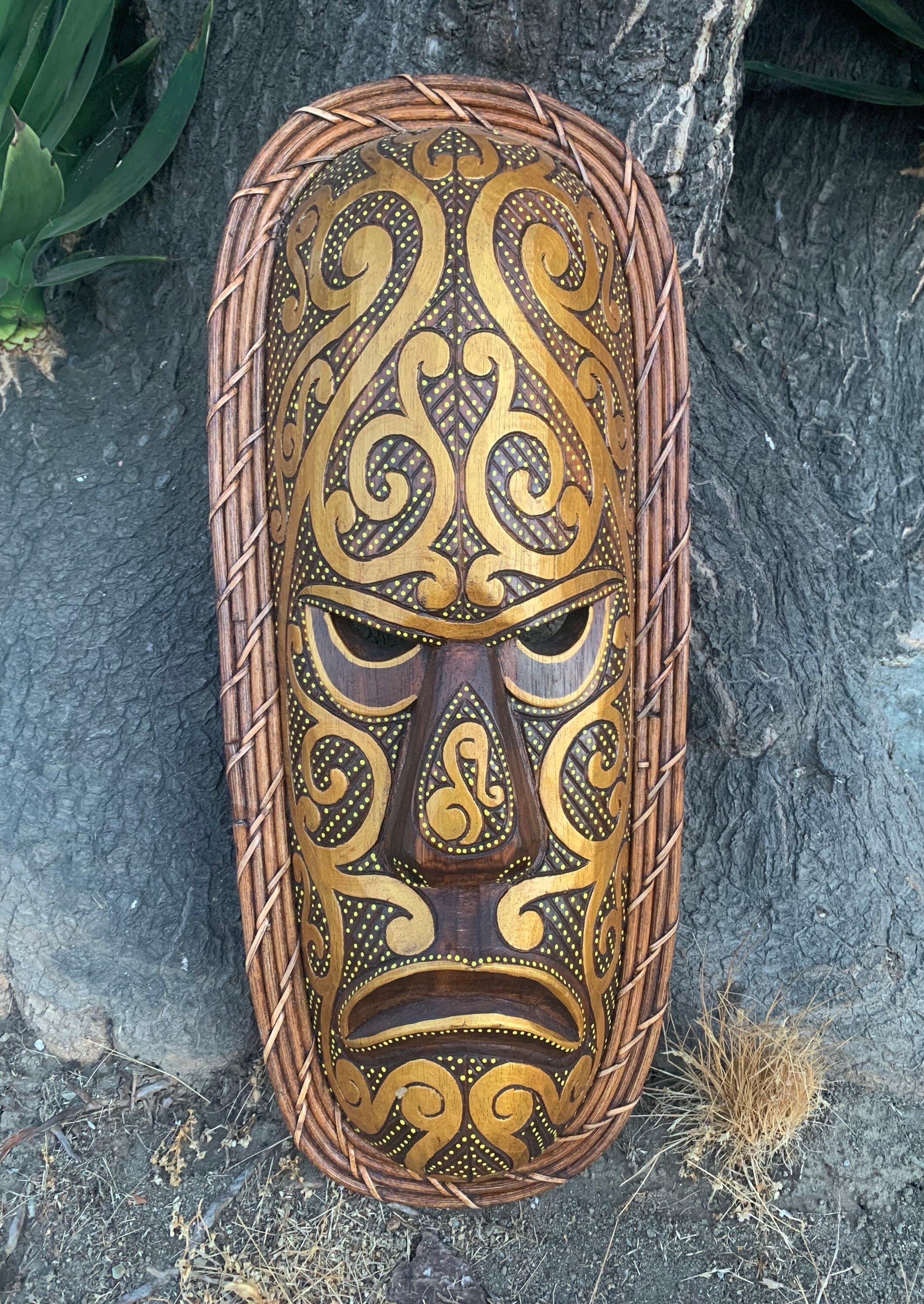 Intricately carved wooden mask with gold scrollwork and dotted details framed by woven wicker.
