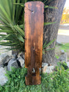 Rustic weathered wooden signboard leaning against a tree with arched-cut base