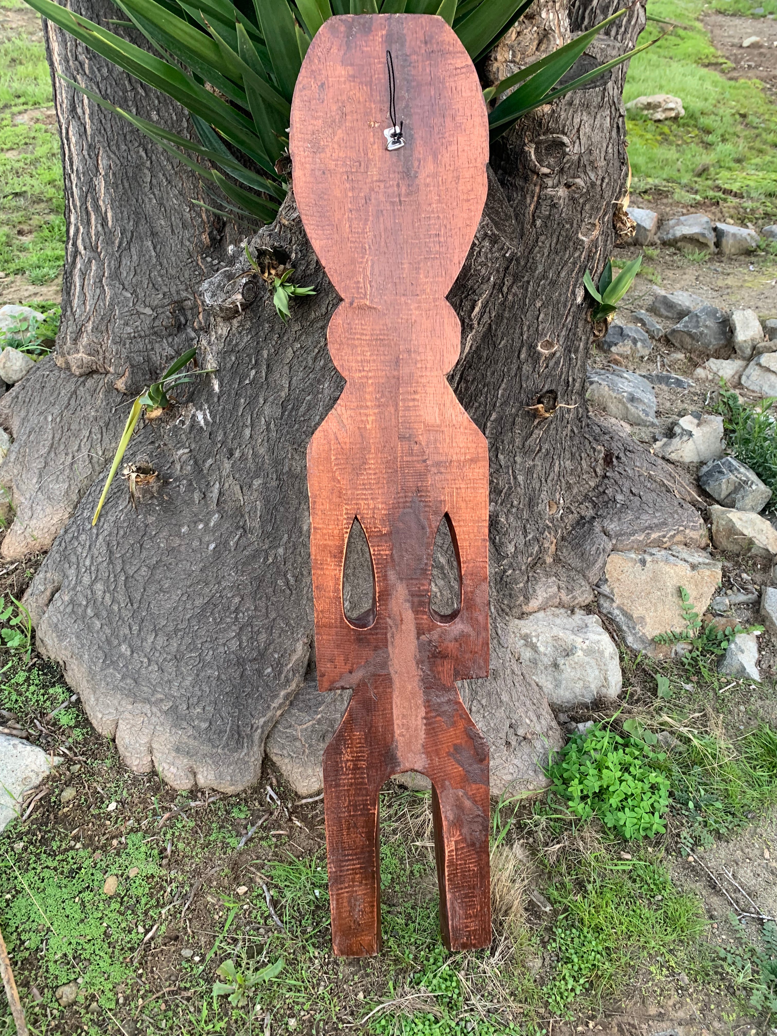 Rustic wooden abstract humanoid sculpture leaning against a tree trunk