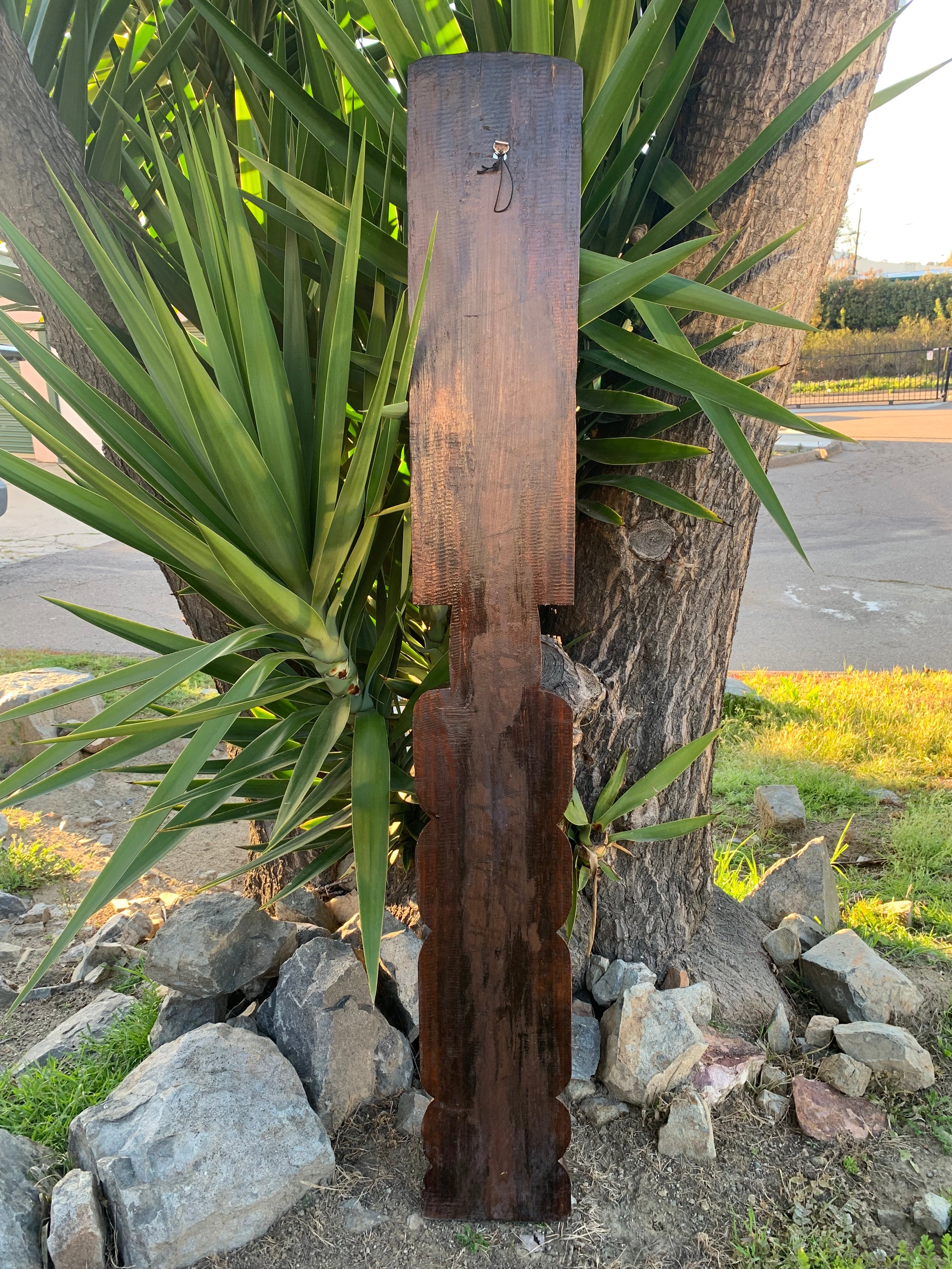 Rustic dark wooden signpost leaning against a tree beside spiky green plants and rocks