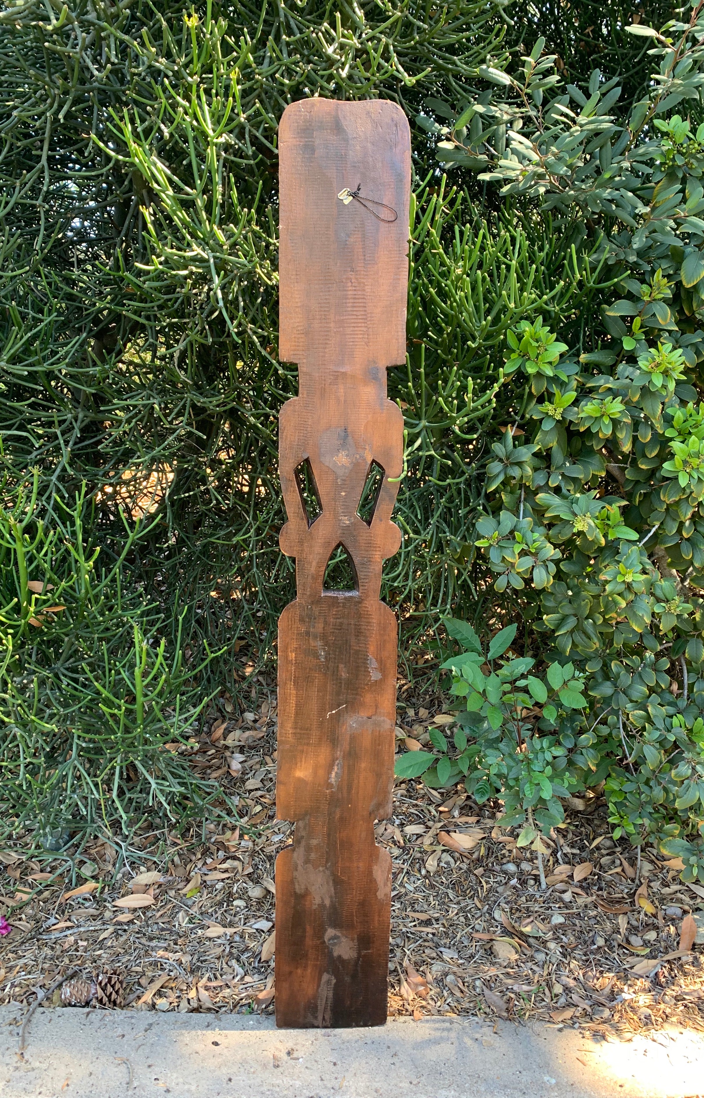 Tall rustic wooden totem sculpture with cutouts in a garden.