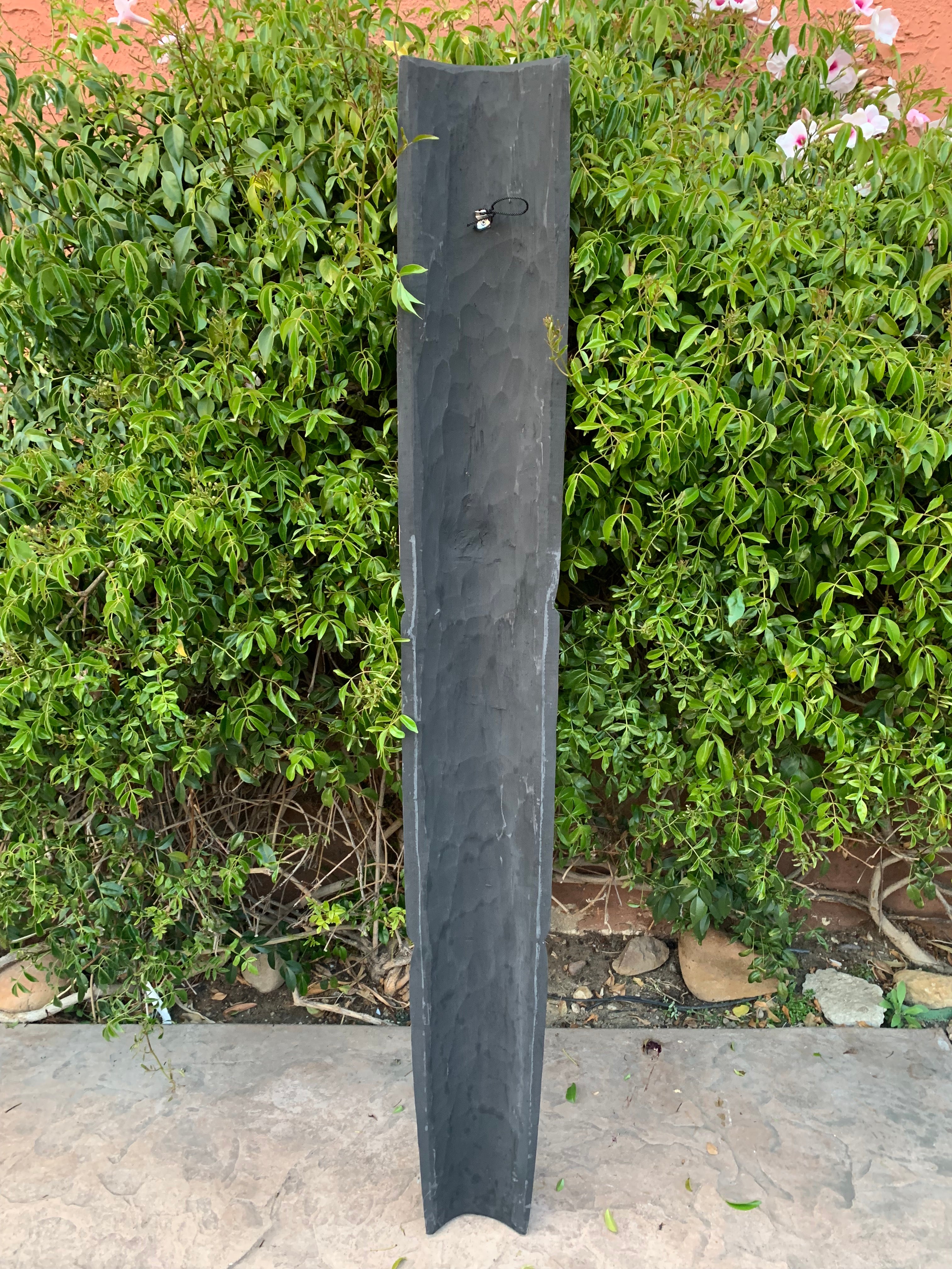 Tall dark slate garden post on a stone patio with green hedge behind