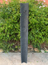 Tall dark slate garden post on a stone patio with green hedge behind