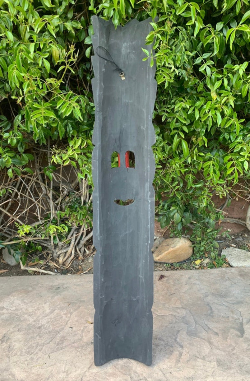 Slate vertical outdoor sculpture with face-like cutouts against greenery